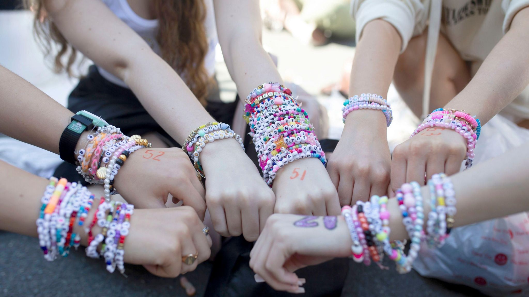 Seven hands together in a circle, showing off the multiple friendship bracelets on the wearers' wrists