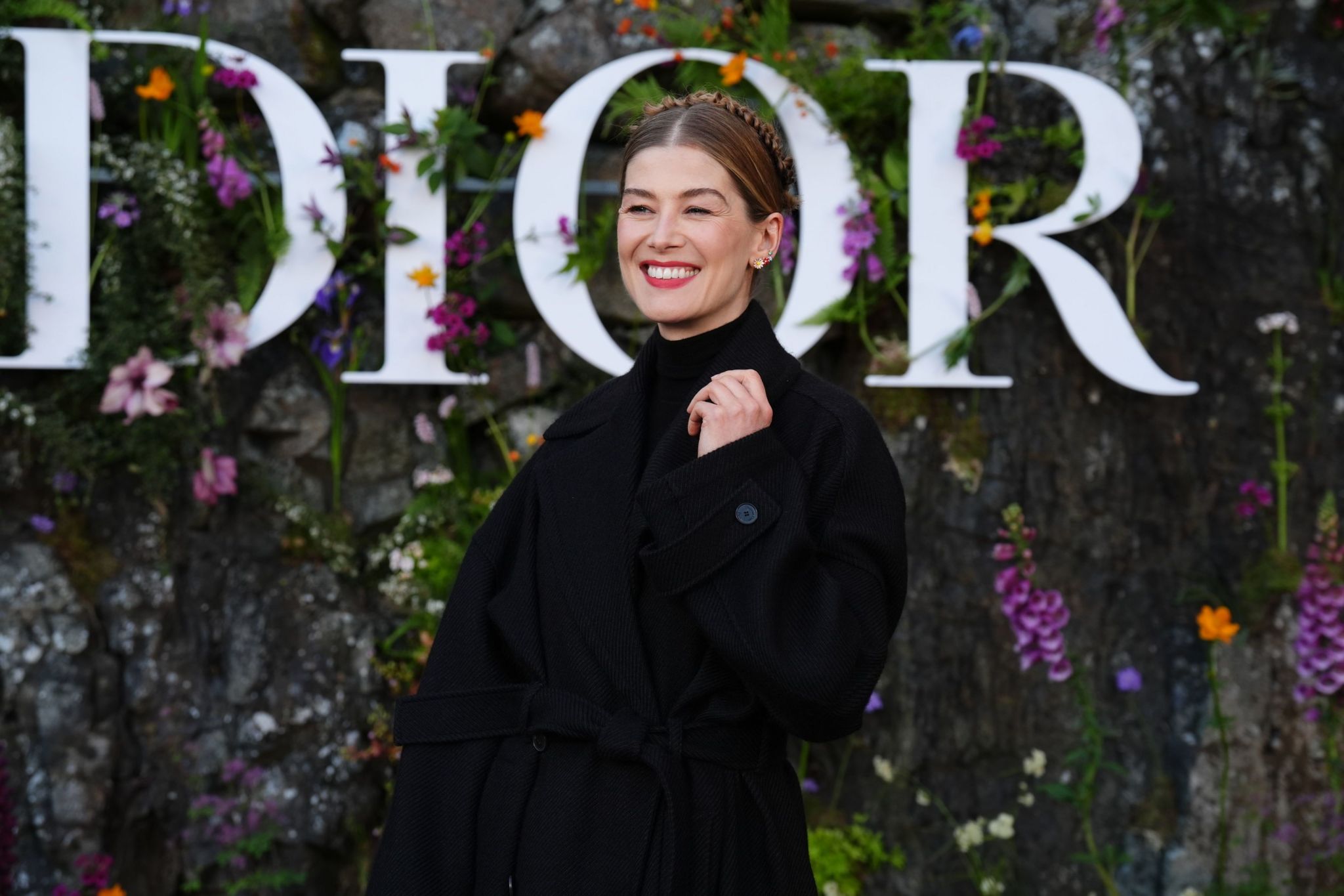Rosamund Pike wearing a slouchy belted trench coat over a black turtleneck at the Dior catwalk