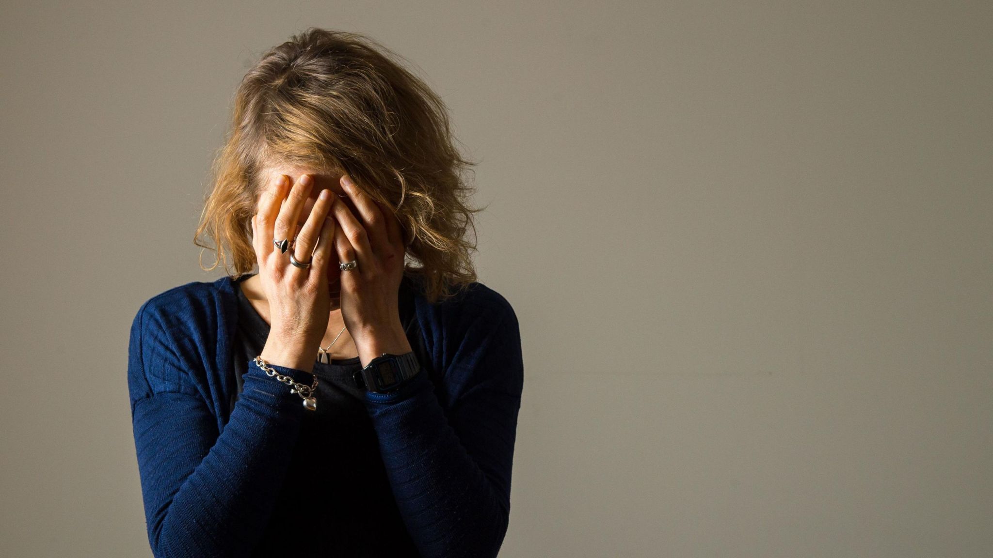 A woman wearing a blue jumper holds her head in her hands as she struggles to cope with the symptoms of the menopause  