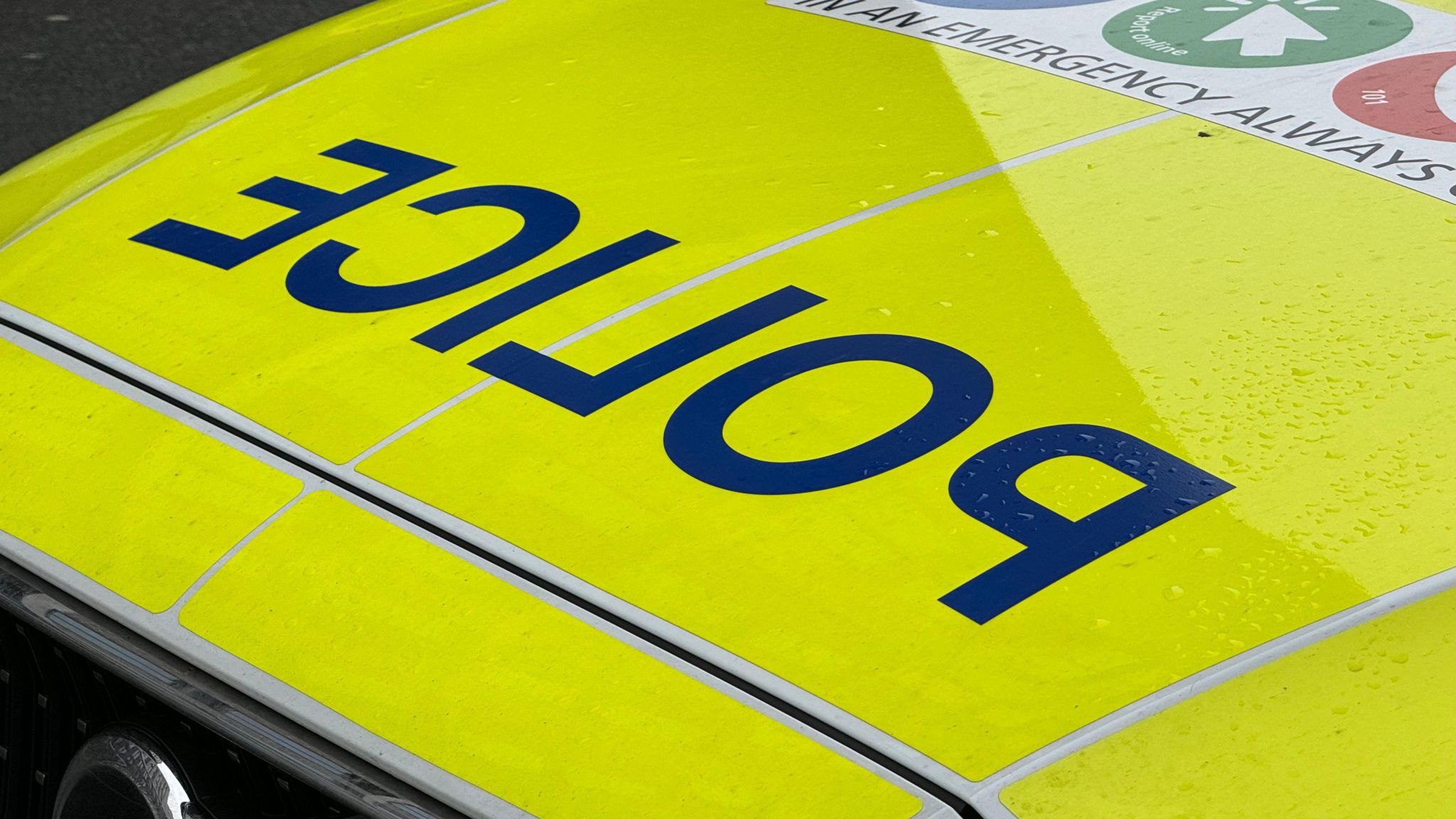 The bonnet of a police car with dark blue reversed letters that read 'police' on a fluorescent yellow backdrop