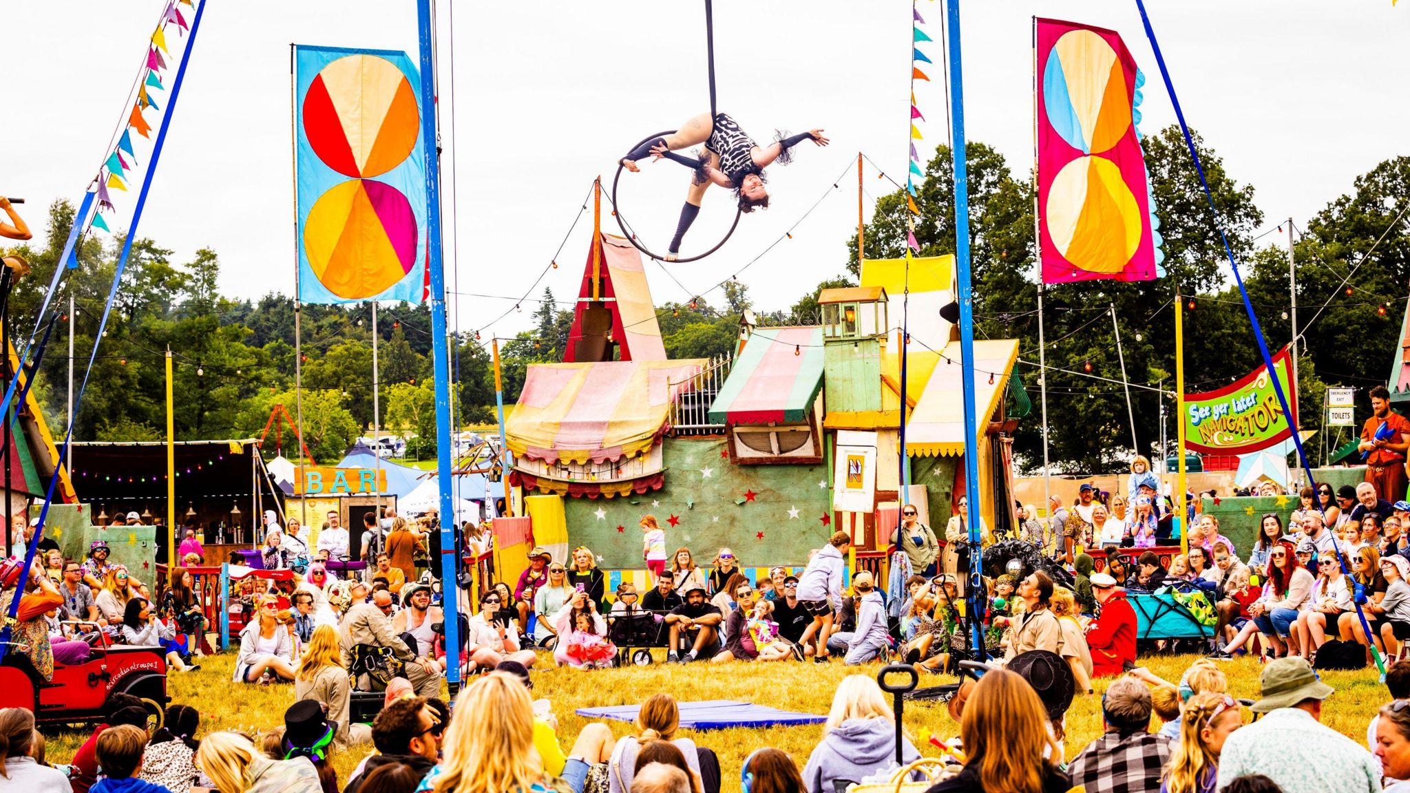 A crowd watches on as a person performs acrobatics while suspended in the air on a hoop 