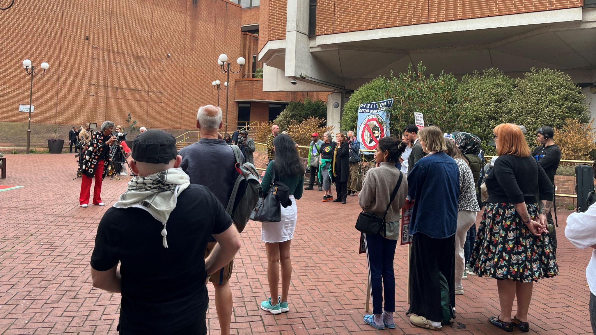 About a dozen people are pictured gathered outside Kensington Town Hall after the long-awaited report into the Grenfell Tower fire was published on Wednesday. Some are holding banners and posters, but most are looking towards one woman at the front who is speaking.