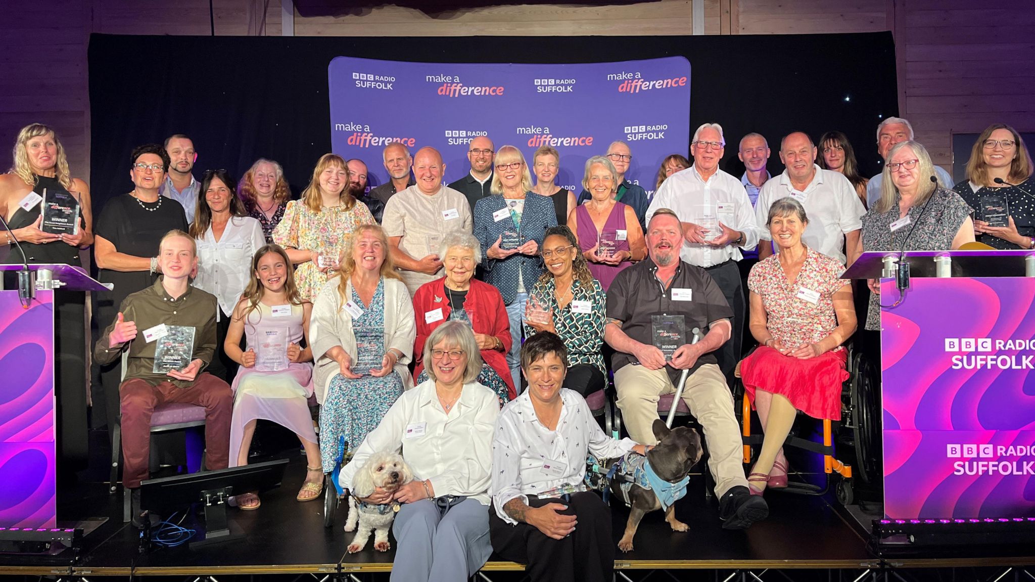 A stage full of people with trophies. In the foreground are two dogs.