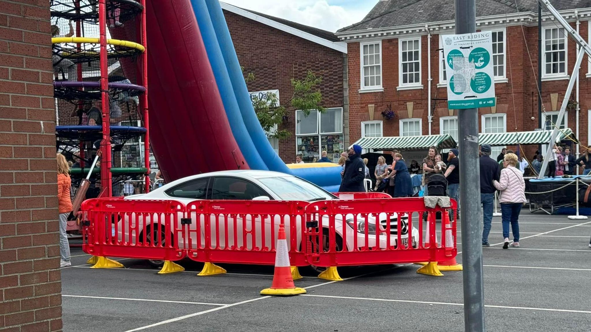 A white Mercedes car is surrounded by red barriers at the Cottingham Day festival