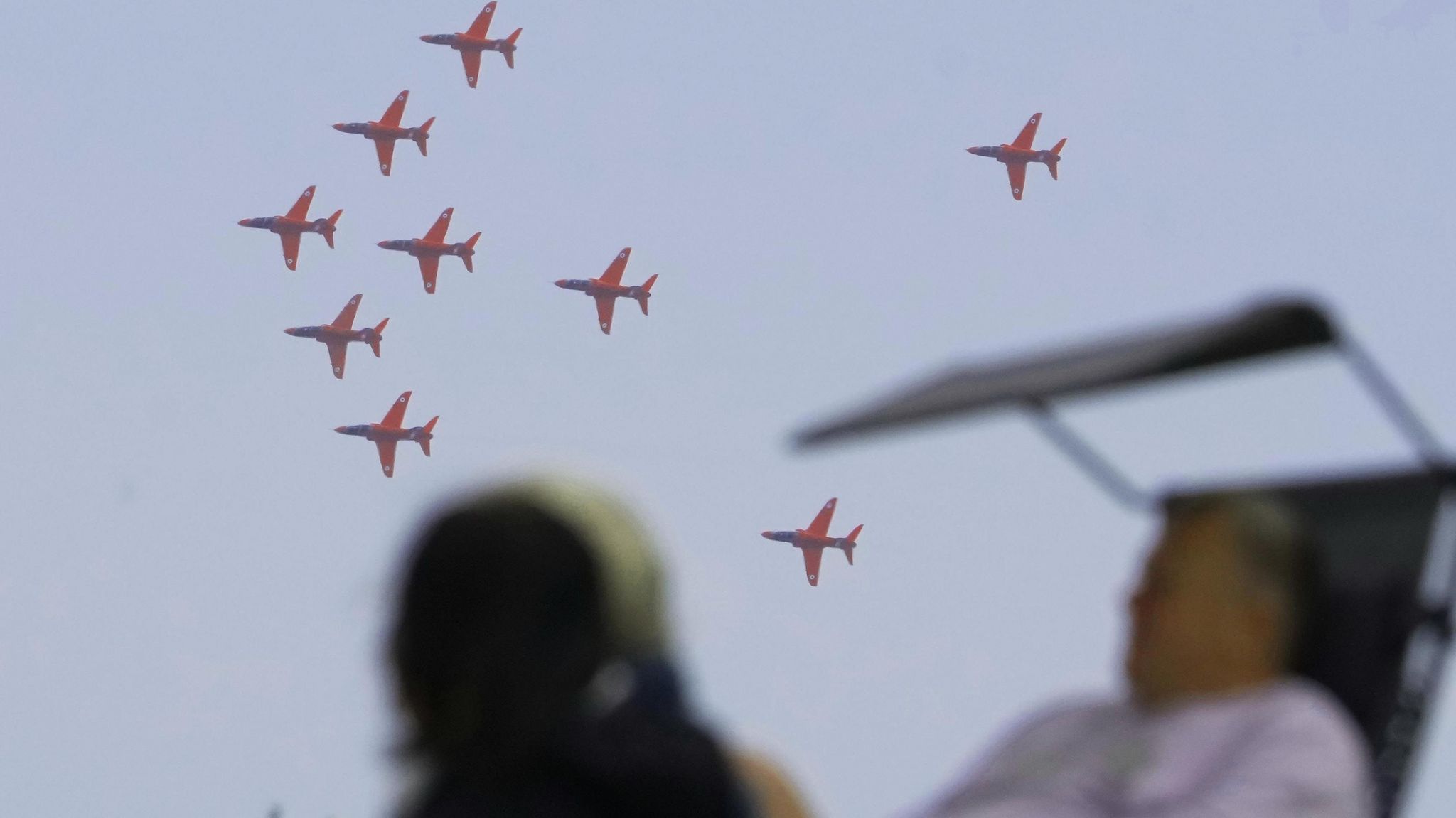 People watch a formation of planes flying in the sky. 