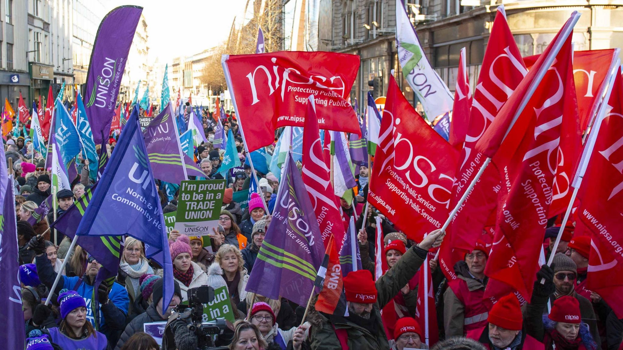 Hundreds of people from different trade unions stand in a Belfast street waving red, blue, purple and green flags