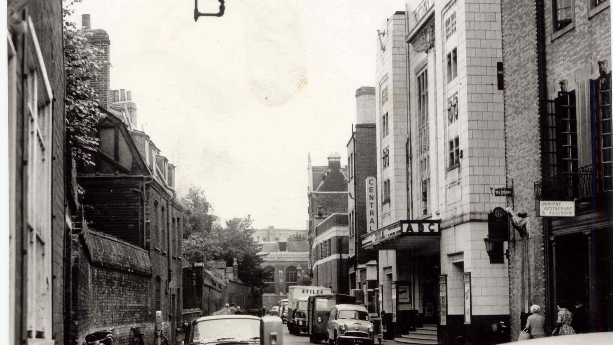 Black and white photo showing Hobson Street in the 1960s with two cars, a parking meter and lamp on the left and on the right the cinema building, which has a sign on it saying Central Cinema ABC in capital letters