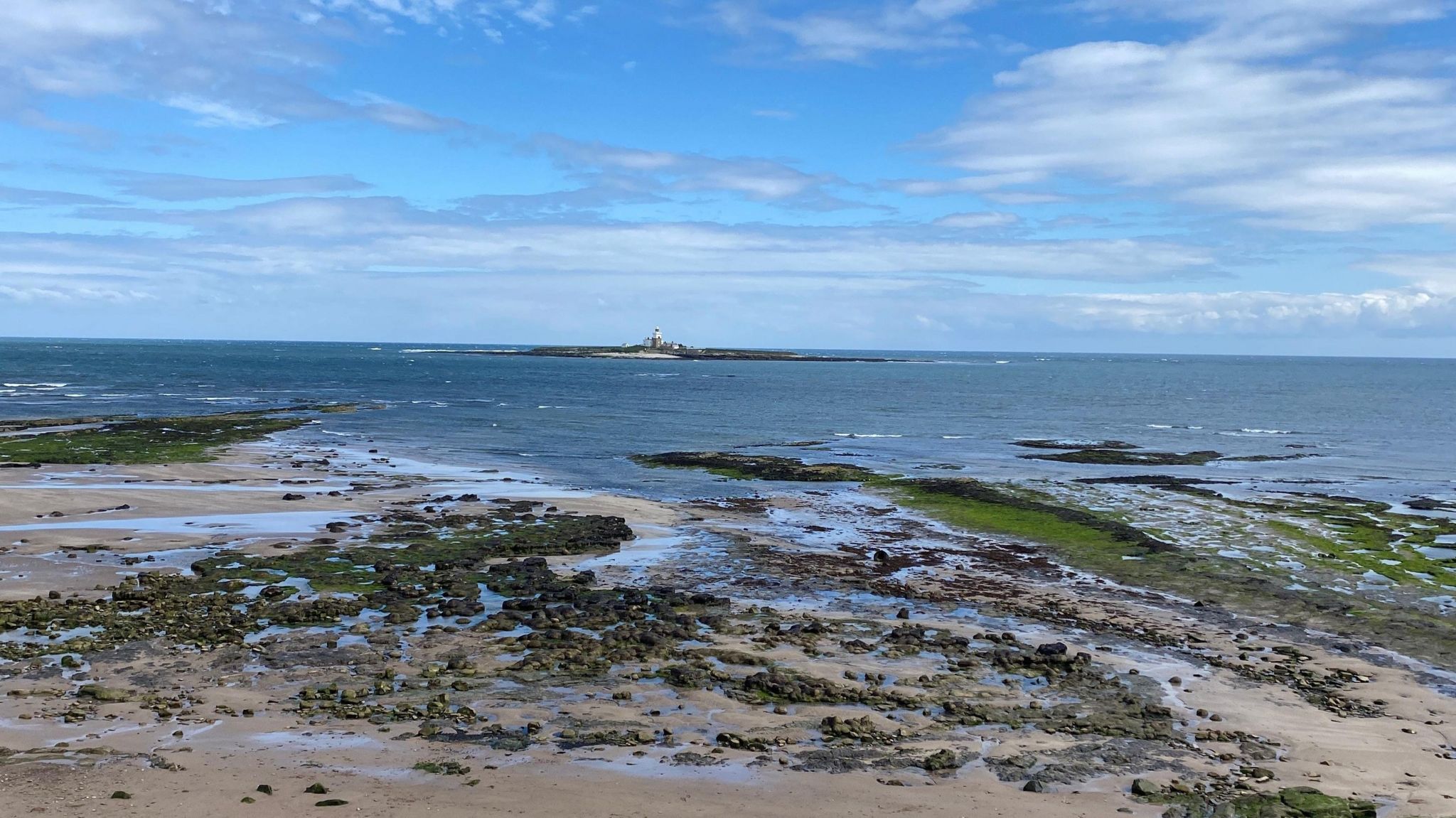 Coquet island from the beach with a blue sky above 