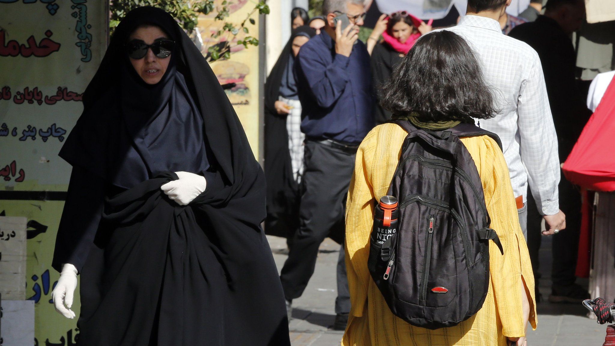 A girl with her hair uncovered walks past a veiled woman on a street in Tehran, Iran (13 September 2023)