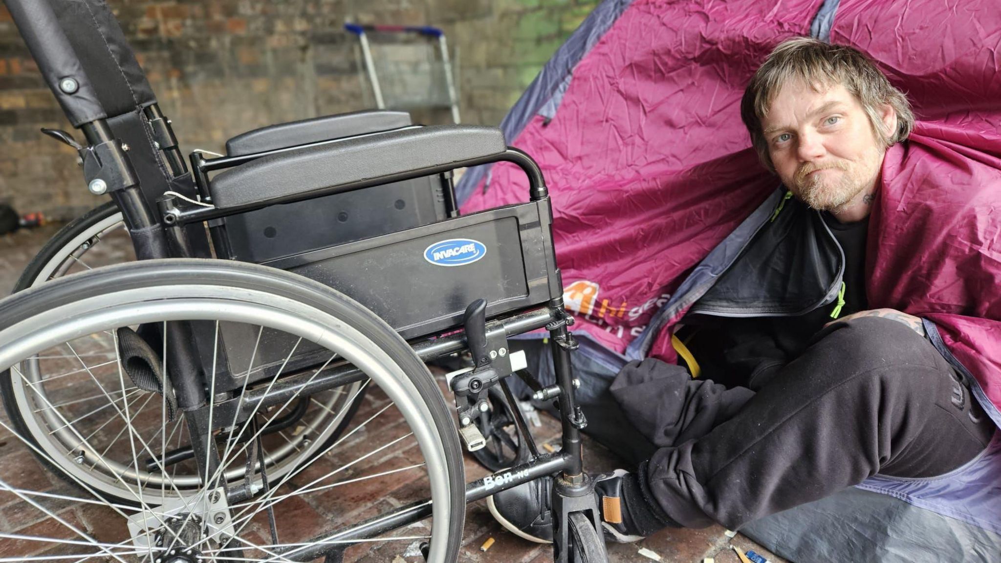 A man in a tent sat next to a wheelchair in Bradford