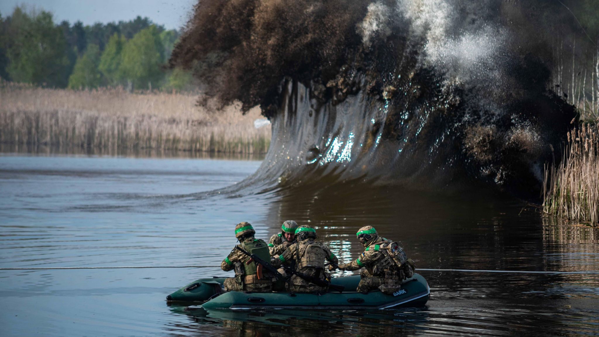 Soldiers bracing on a raft after an explosion hits the water