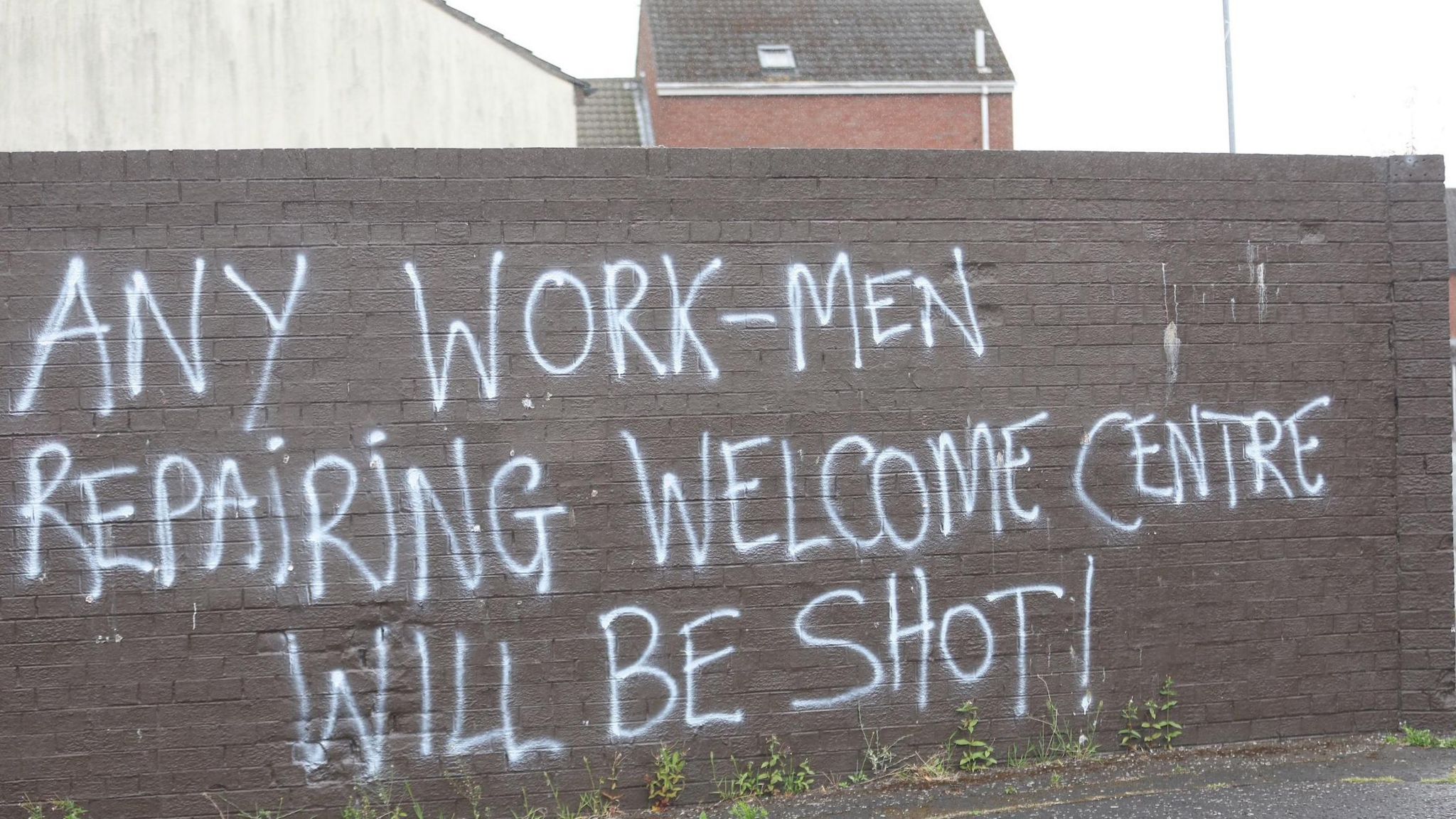 Graffiti on wall saying:" Any work-men repairing Welcome Centre will be shot!"