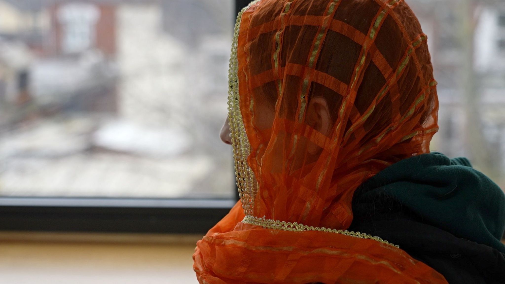 A woman, whose identity cannot be seen, in an orange headscarf looking away from the camera