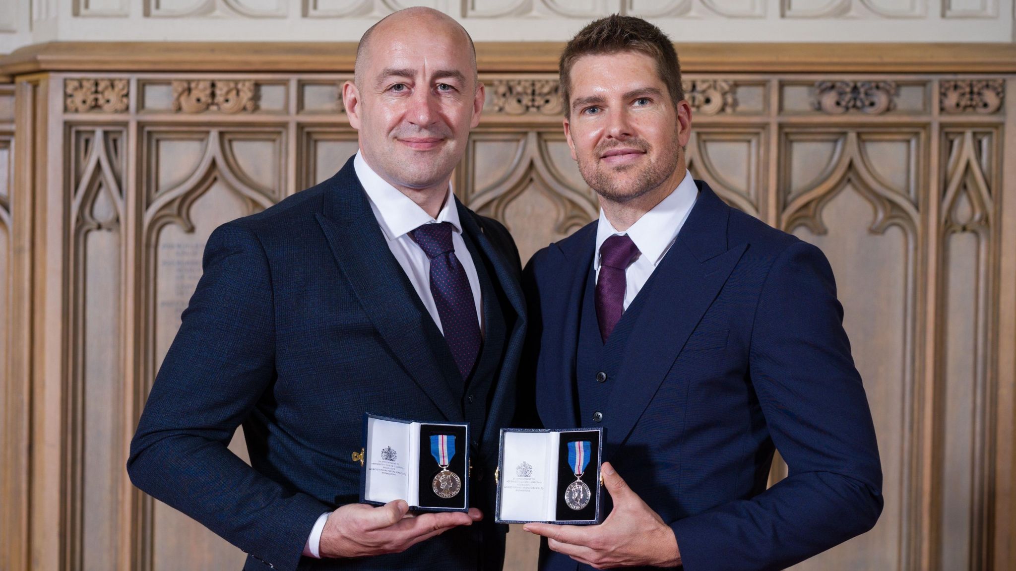 Steve Gallant (l) and Darryn Frost (r) both wear dark blue suits and hold their identical medals in front of them