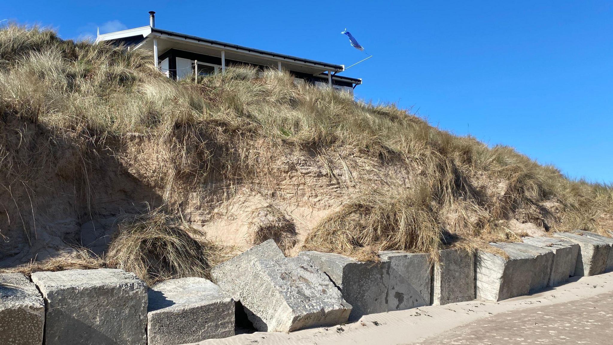 A house above a line of tank traps with an eroded cliff below 