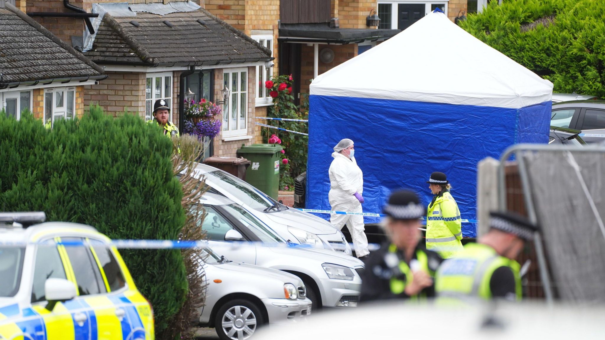 A residential street with a blue forensic tent with police officers and forensic 