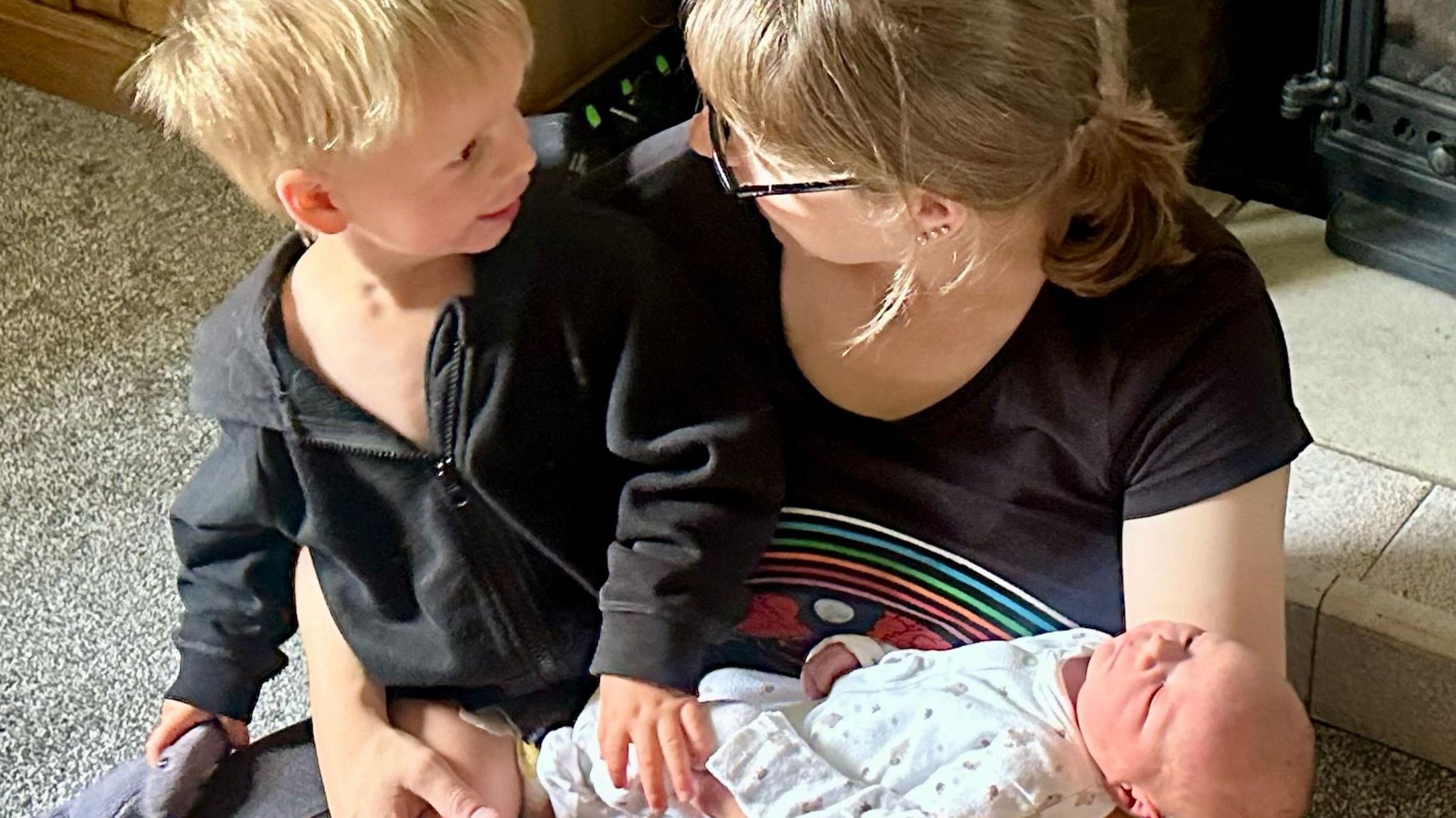 A woman sitting with a two-year-old boy and a newborn baby