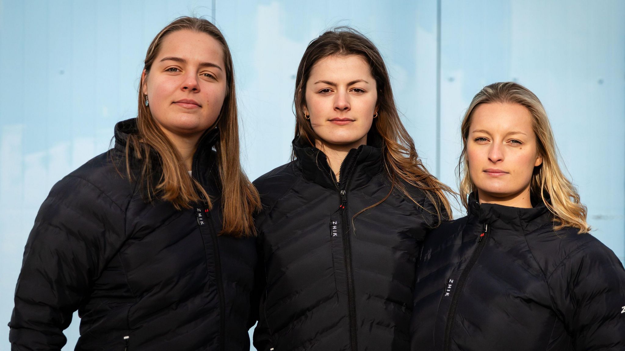 Head and shoulders photo of Lottie Hopkinson-Woolley, Miriam Payne and Jess Rowe standing next to each other wearing identical black sailing jackets