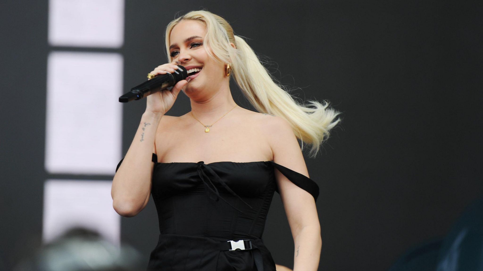 Anne-Marie in a black dress singing into a microphone 