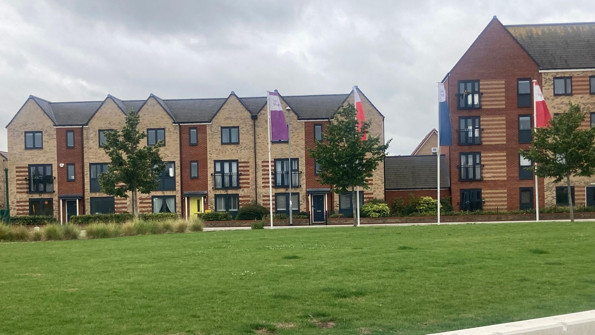 New homes with sales flag in front and a green area in the foreground