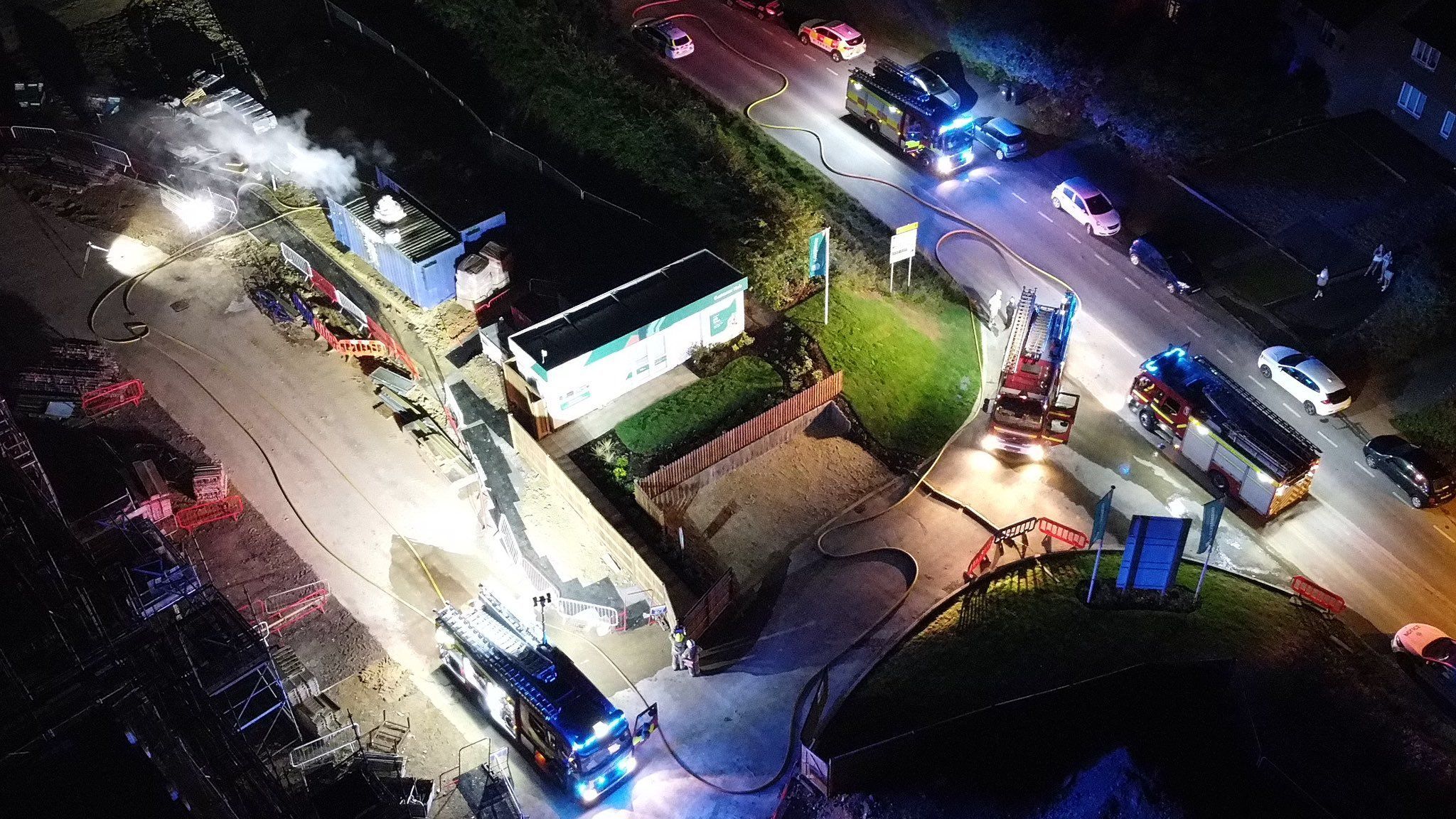 An aerial view of the site shows billowing smoke and containers illuminated in the dark sky