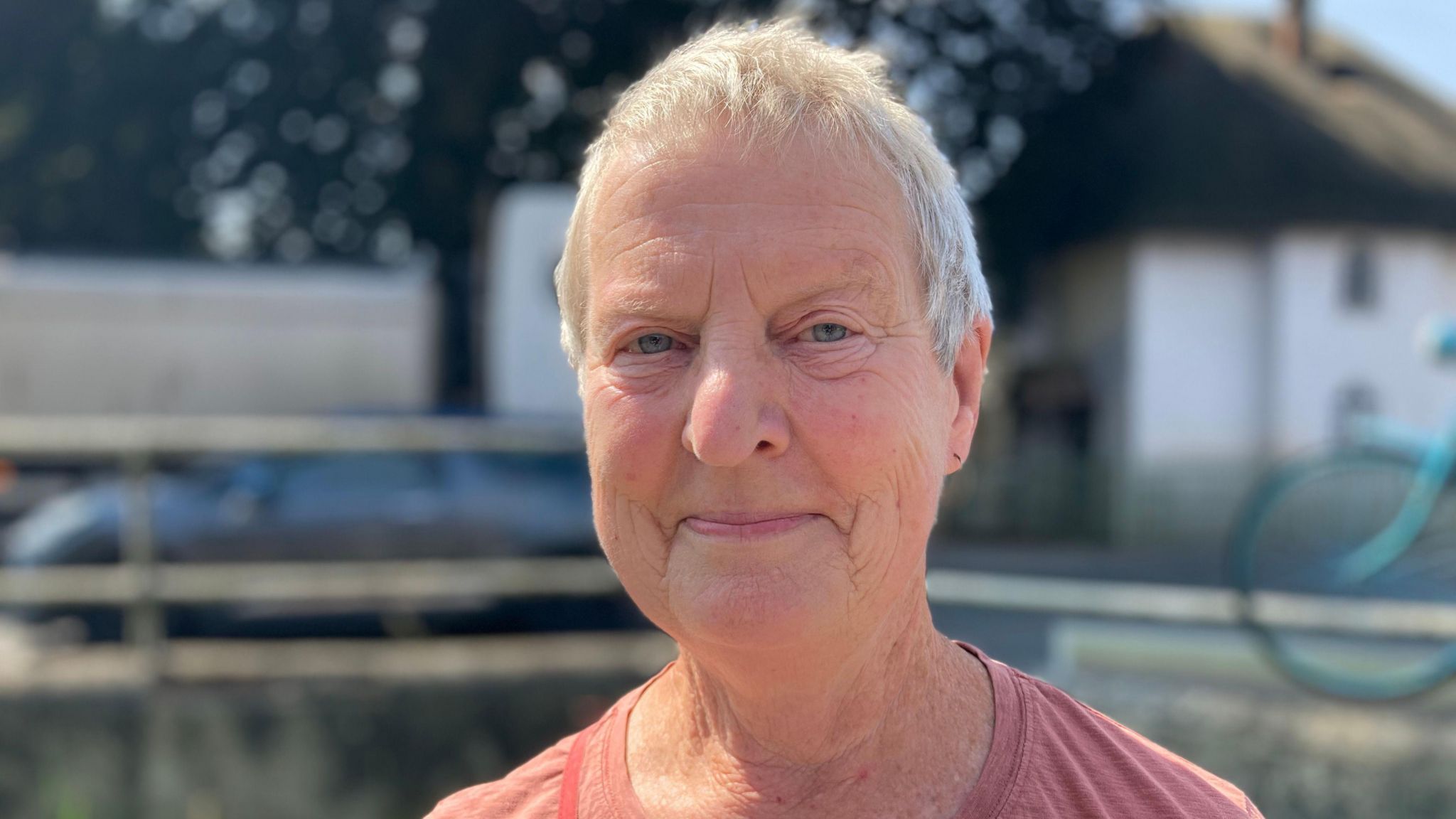 Sharon Paterson looking at the camera on a sunny day. She is wearing a pink top and has short cropped hair