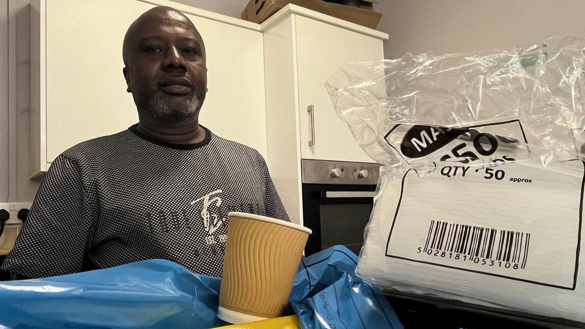 Francis Ahiakpa standing in the kitchen of Humber All Nations Alliance, with a stack of takeaway containers