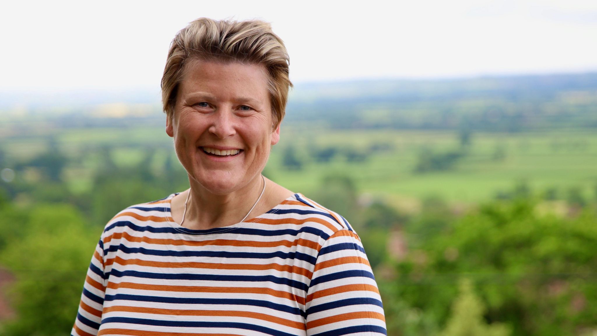 Sarah Dyke looking at the camera in front of a pretty view in Somerset