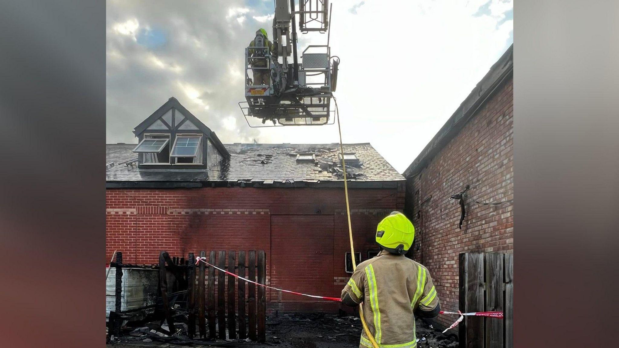 Firefighters operating a crane over a burnt roof