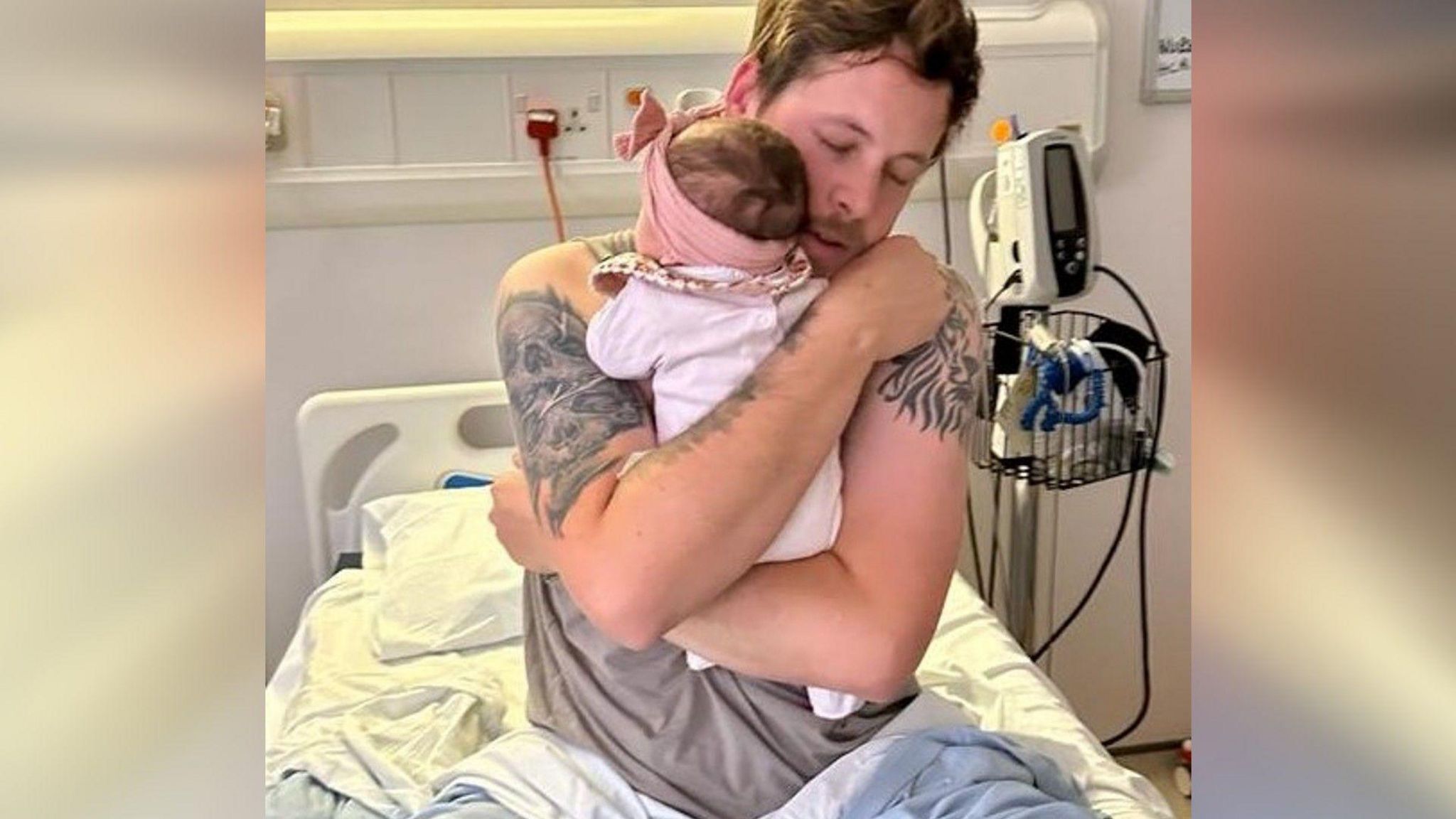 Sam hugging his daughter while sitting in a hospital bed