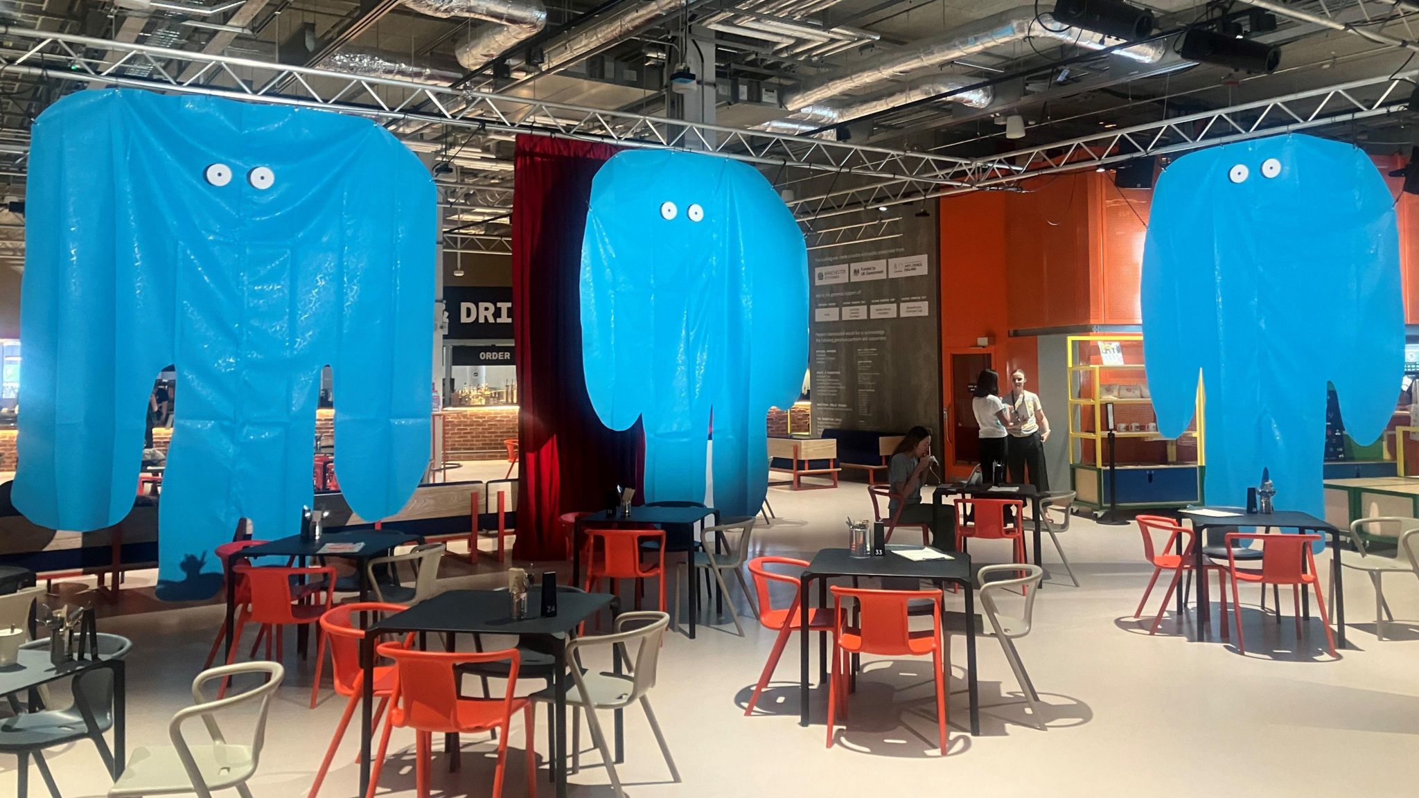 Blue inflatable monsters hang from a ceiling above a cafe at Aviva Studios 