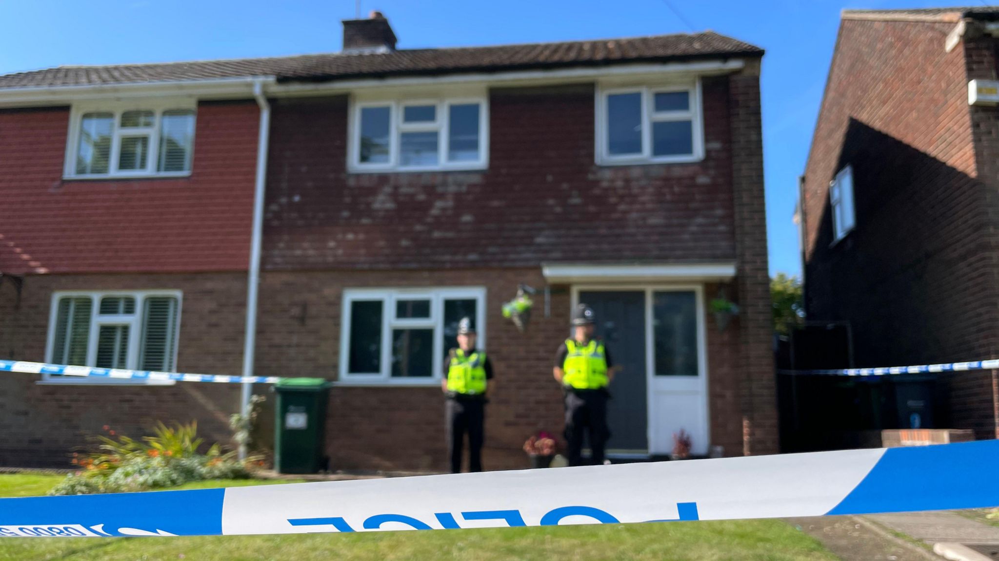 Police officers in uniform stand in front of a house cordoned off by police