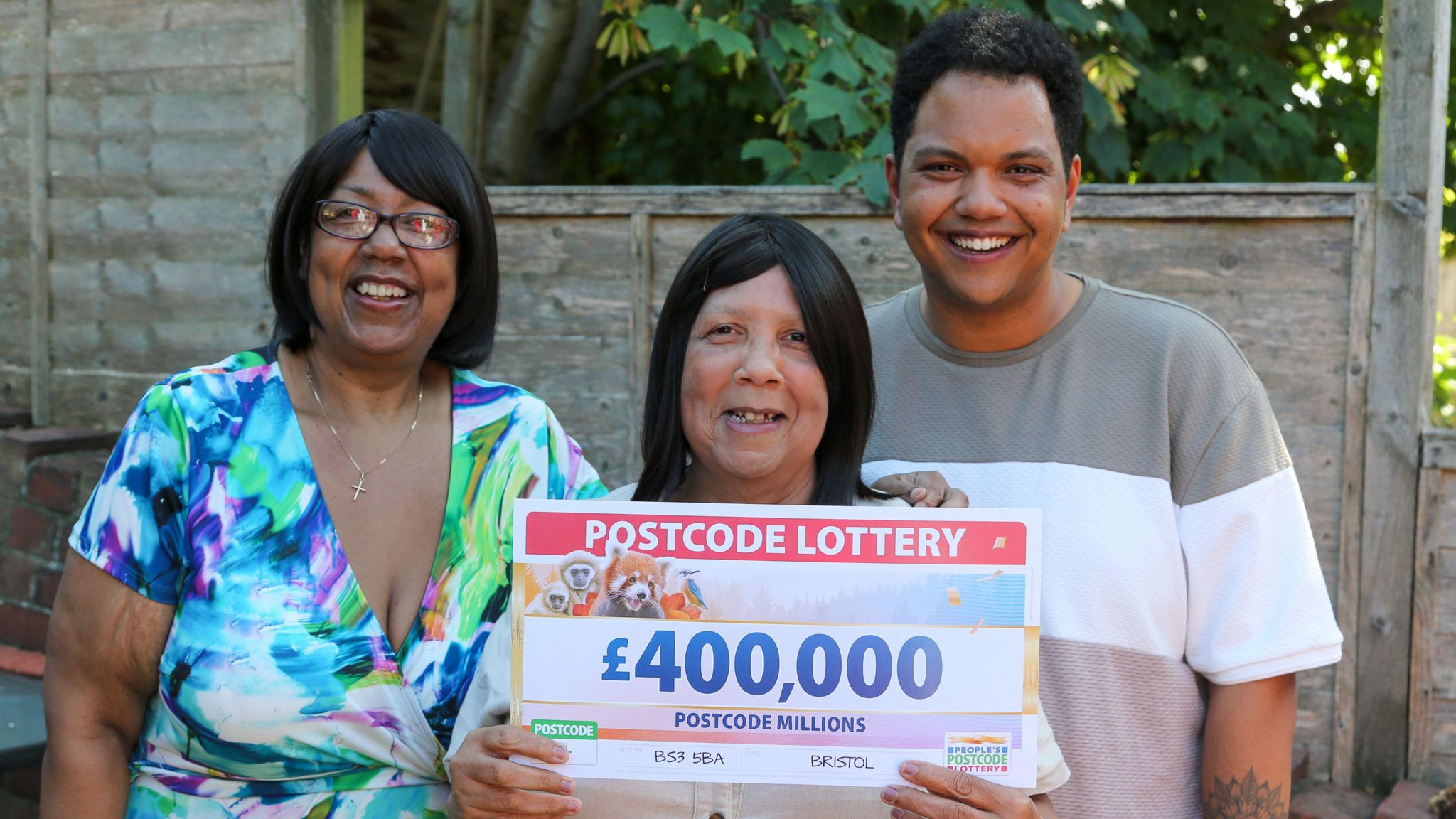 (L-R) Catherine Joseph, wearing a white flowery dress, Celestina Joseph, holding a big cheque with £400,000 written on it,  and Jack Joseph, wearing a striped grey, white and pink t-shirt.