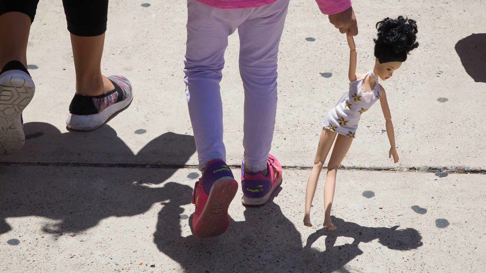 A 4-year-old Honduran girl carries a doll while walking with her immigrant mother