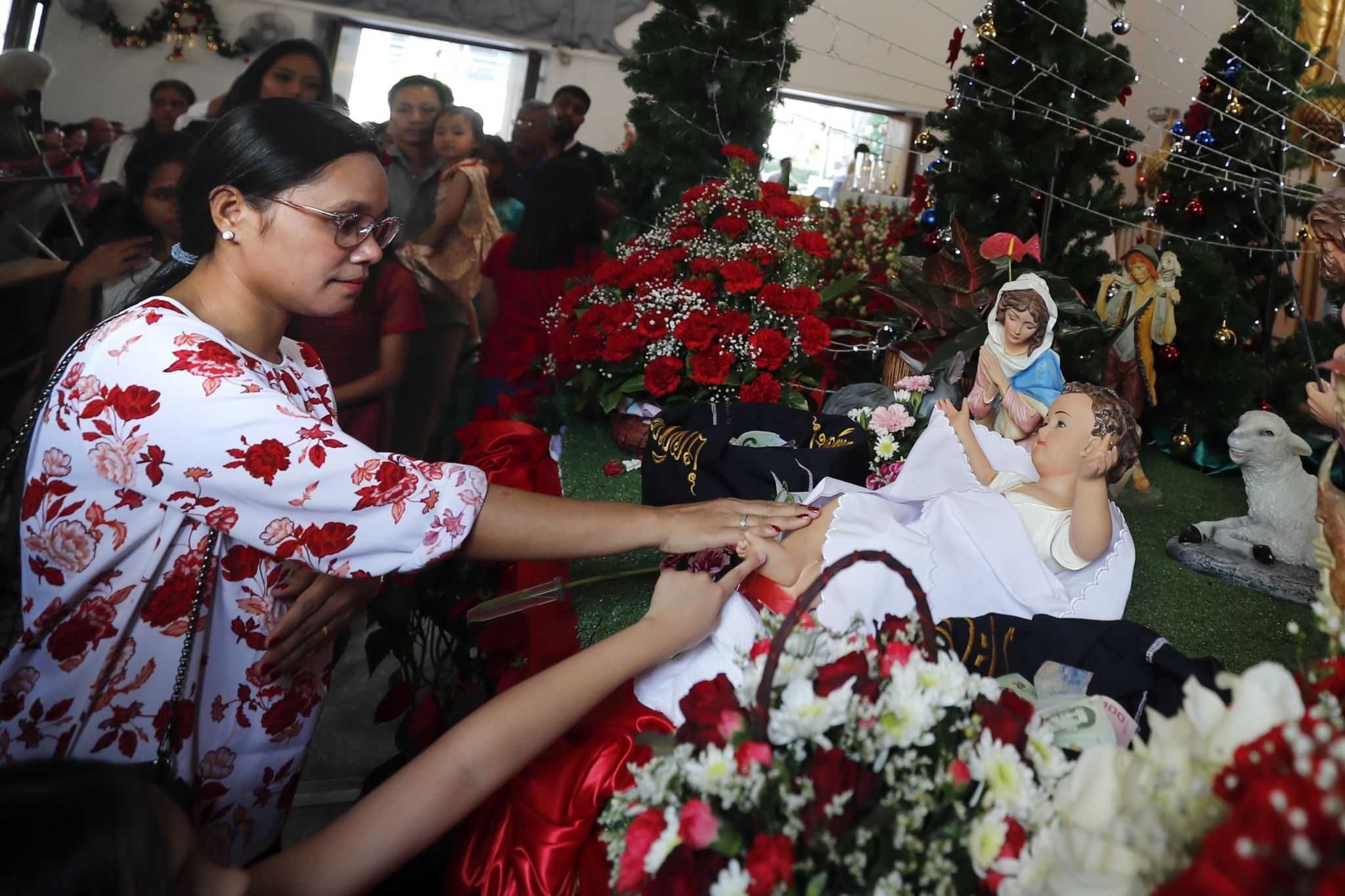 Thai and foreign Catholic church goers touch the baby Jesus doll in the Nativity scene during Christmas Day Mass at a church in Bangkok