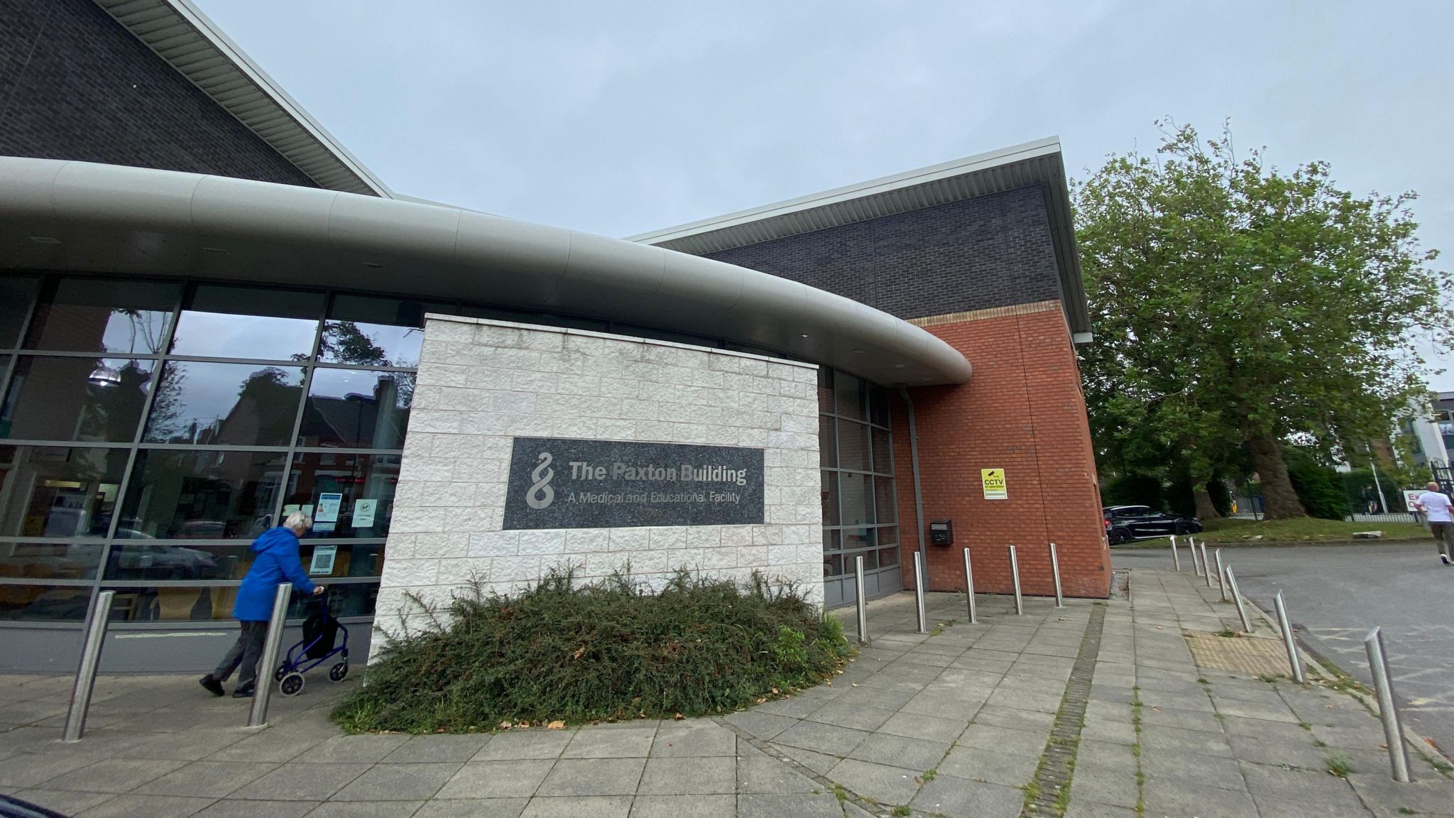 An outside shot of The Paxton Medical Group site. It is a modern curved design with light grey brickwork, windows, and a large pavement outside.