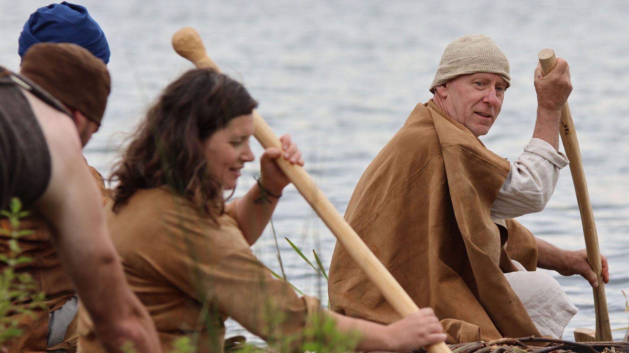 Two men and a woman in bronze age costume row a boat