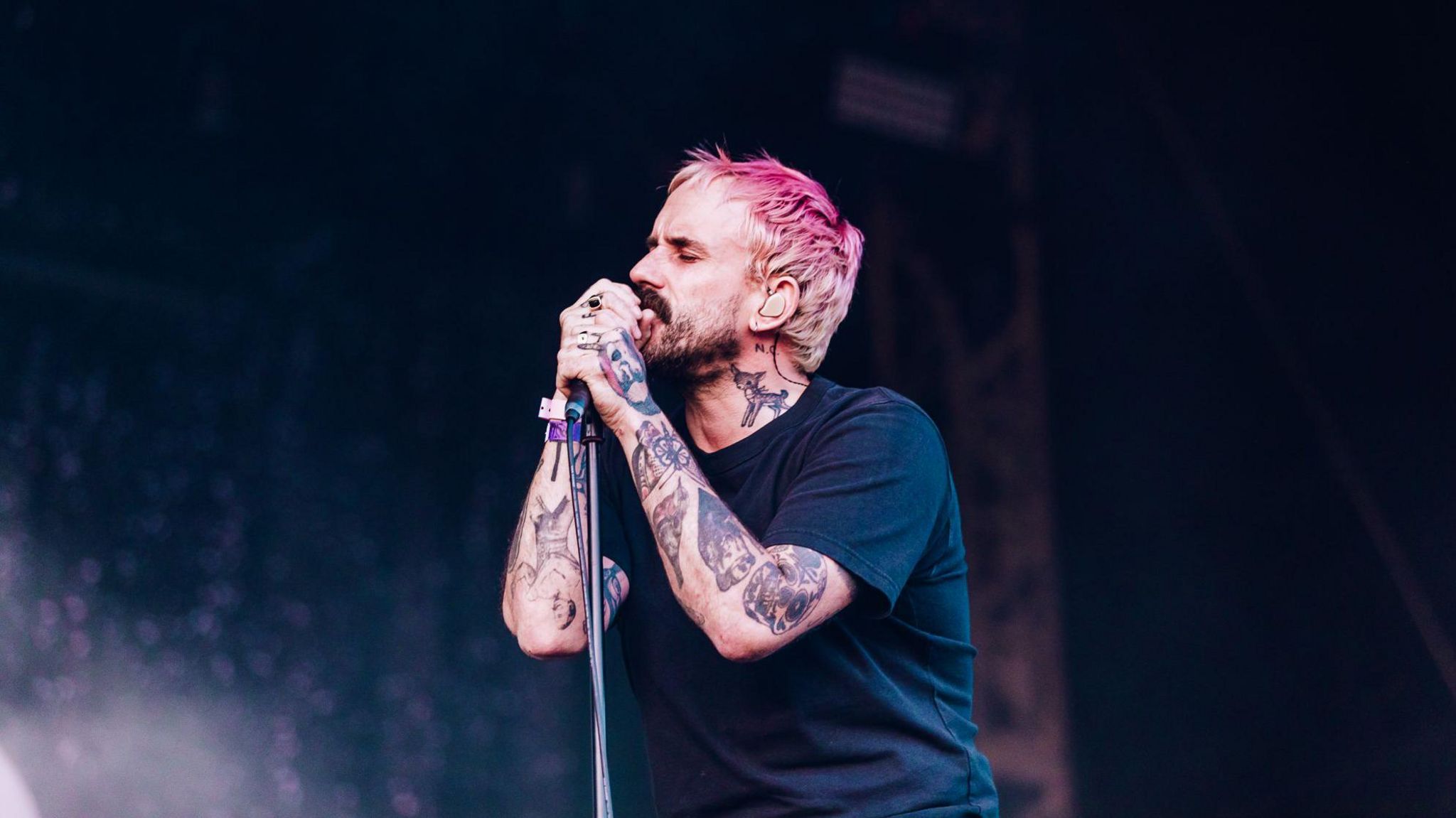 Joe Talbot sings on stage, his eyes closed. Mr Talbot has pink hair and tattoos on his neck and shoulders.