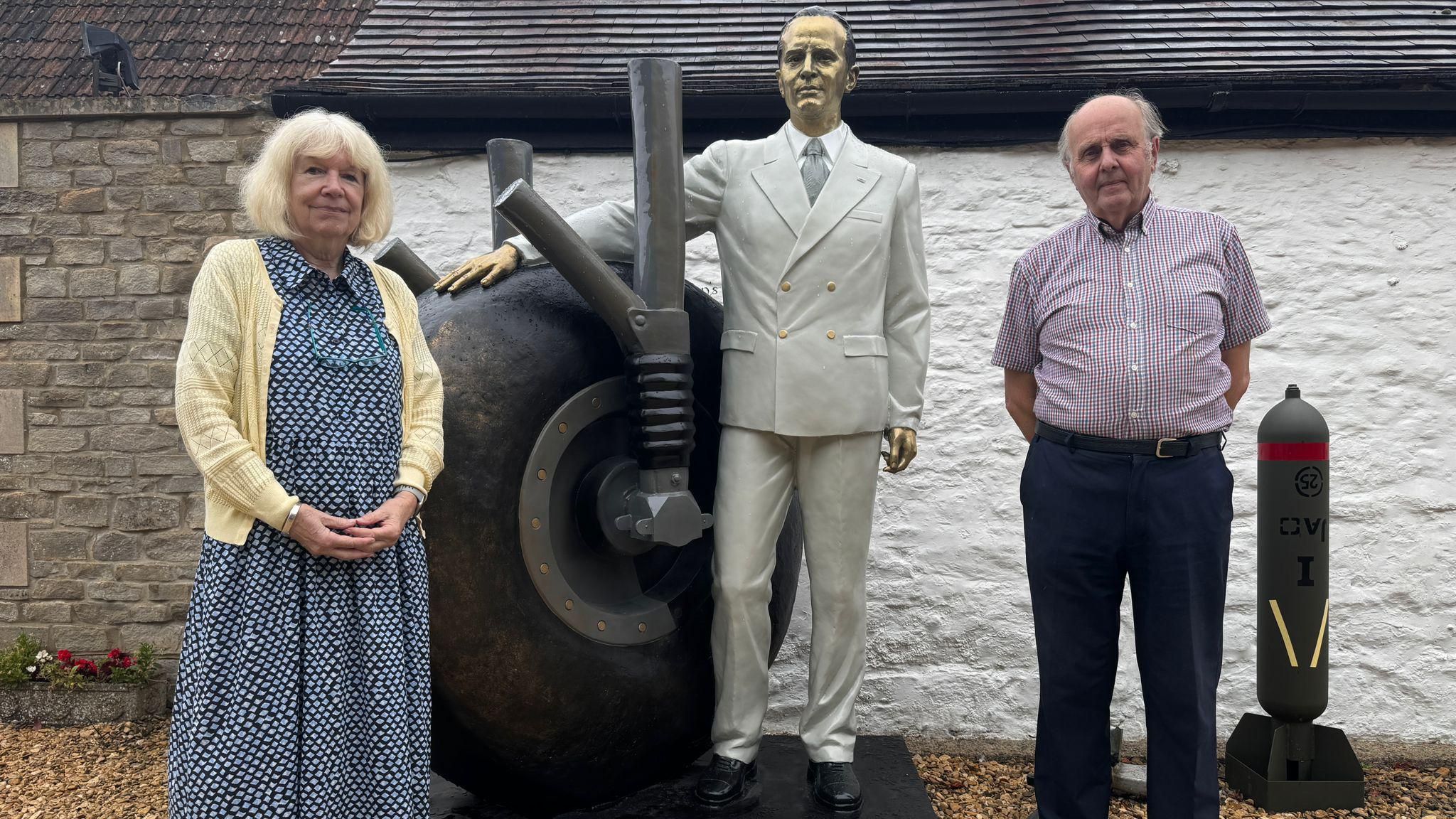 Martin Robins and Caroline Flippants stand next to a bronze statue of Sir George Dowty which depicts him dressed in a light-coloured suit with one hand resting on an aeroplane wheel