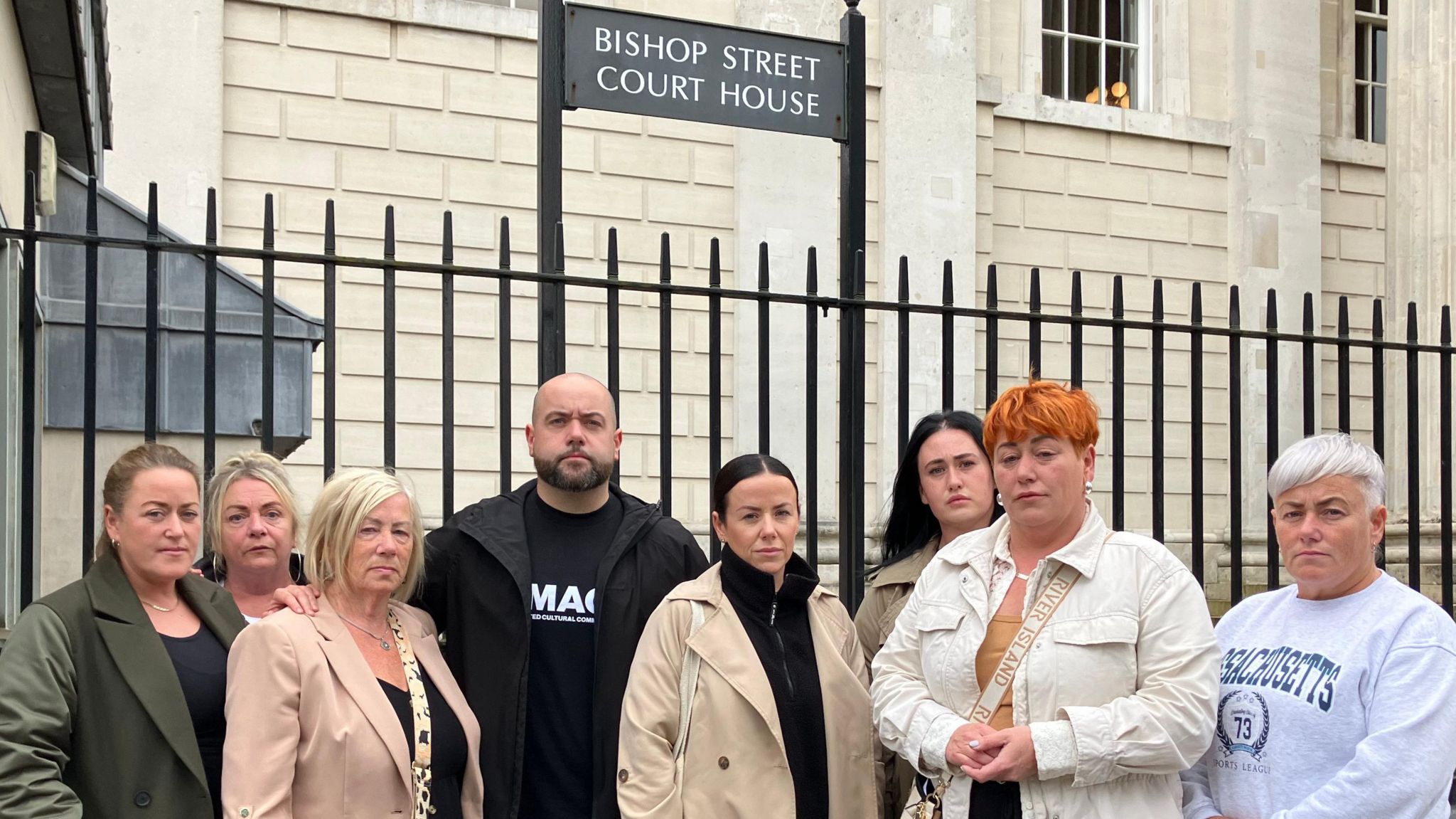 Leanne McLaughlin, the mother of Caitlin, pictured with seven other family members. She is to the left of the image, between two other women, and has medium-length short hair. The group, which features one man and seven woman, all have neutral facial expressions and are standing in front of a fence outside Bishop Street Courthouse in Derry.