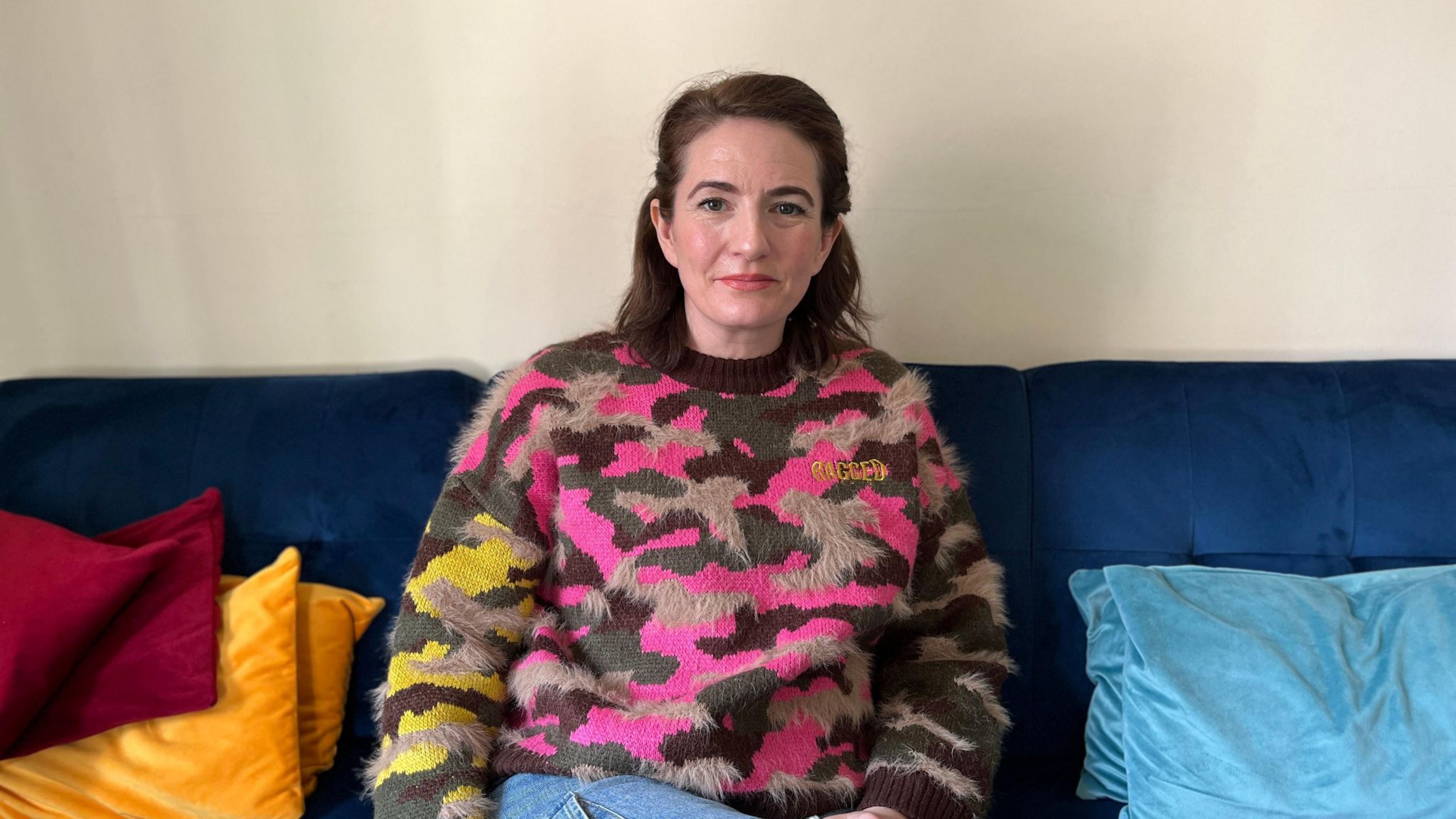 Susie Barrass sat on the sofa in a pink and grey jumper