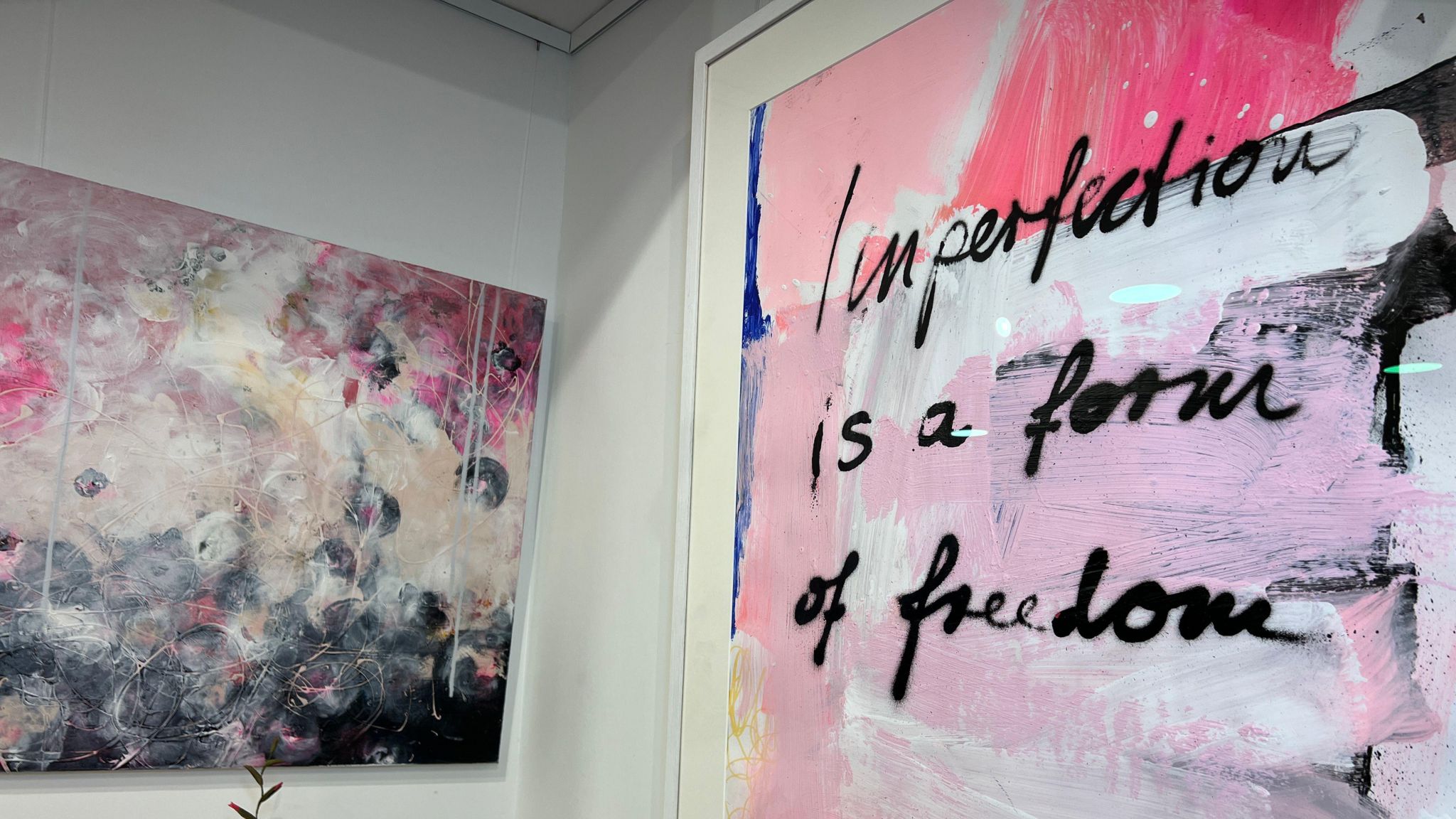 Two pink artworks hang on the wall with one saying imperfection is a form of freedom