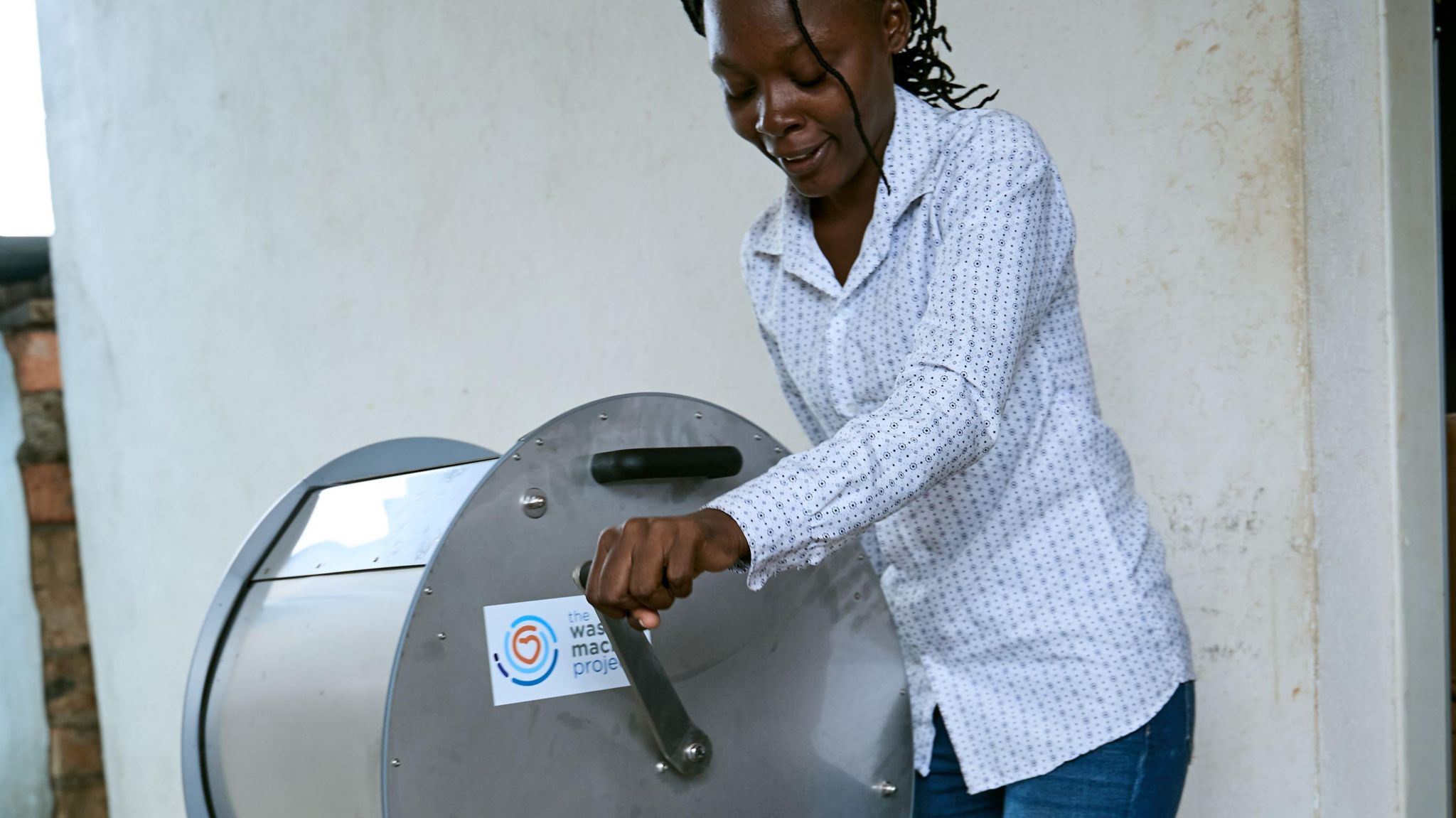 A woman wearing a white shirt twists the handle on one of the manual washing machines