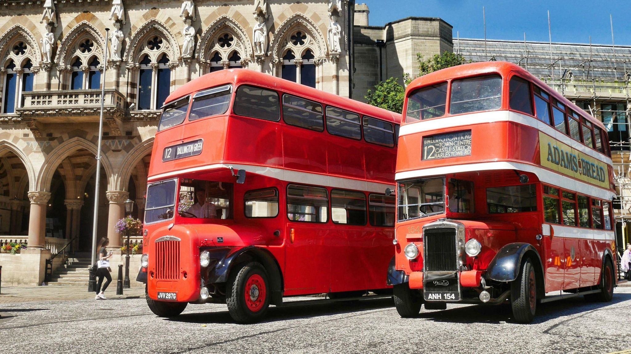 Two red double decker buses with prominent front grilles parked outside Northampton Guildhall