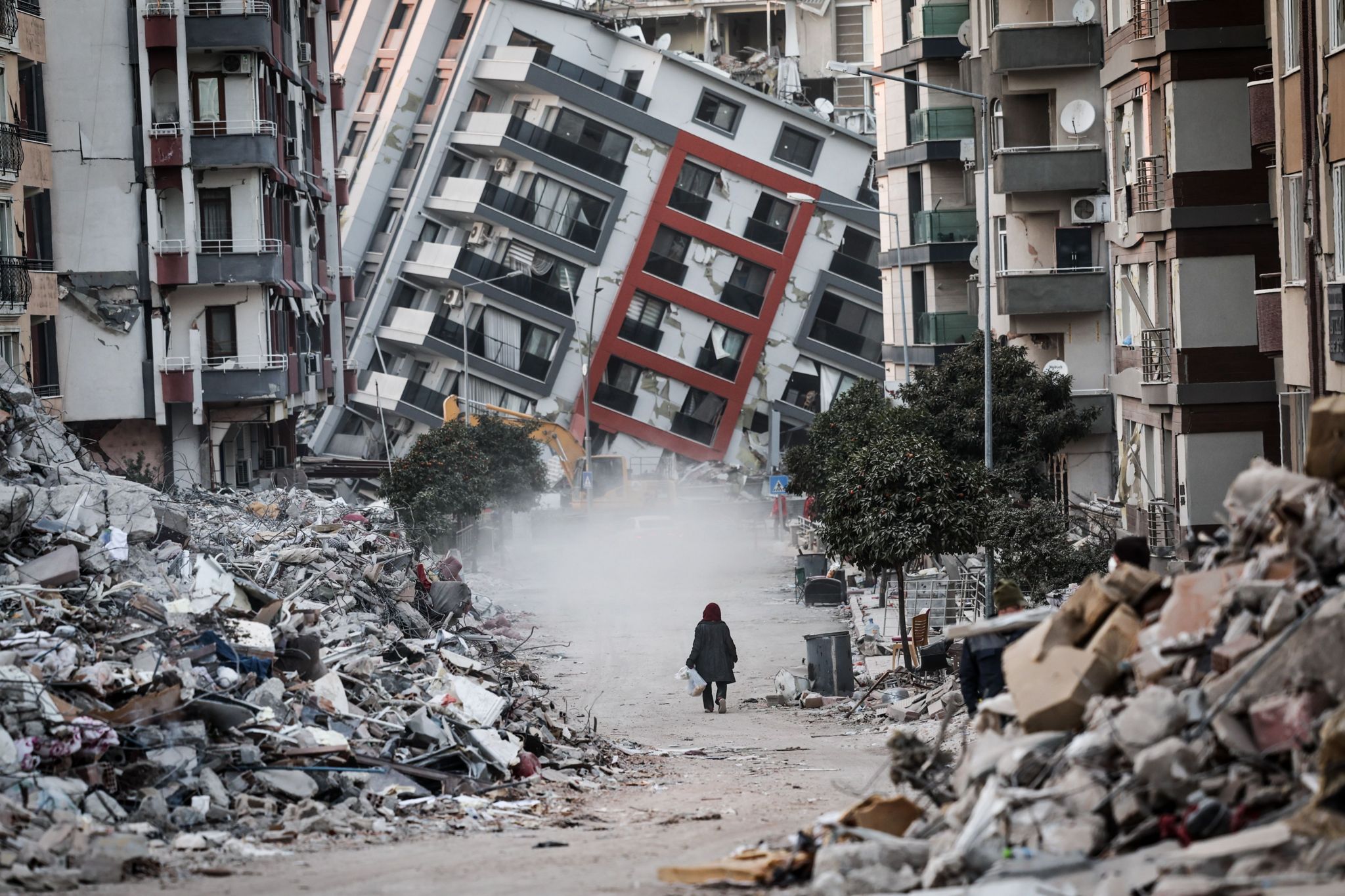 A woman walks in front of a collapsed building while demolition teams work after a powerful earthquake in Hatay, Turkey