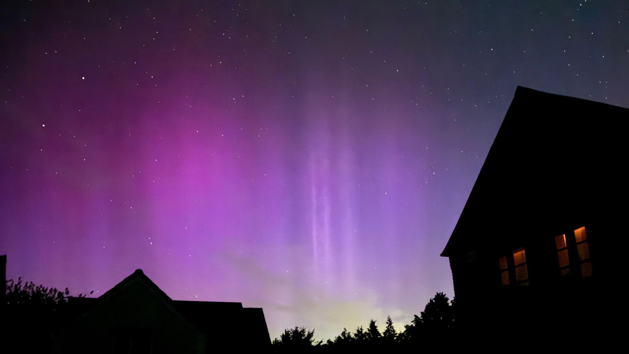 A deep purple sky with flashes of bright lights over silhouetted houses 