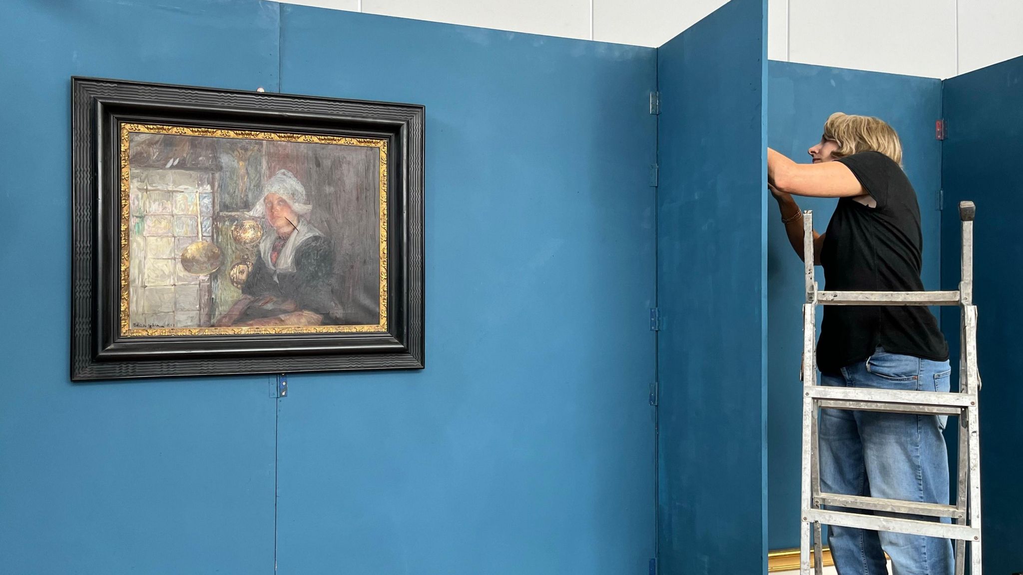 Stabbed painting hangs on gallery wall as curator hangs another picture