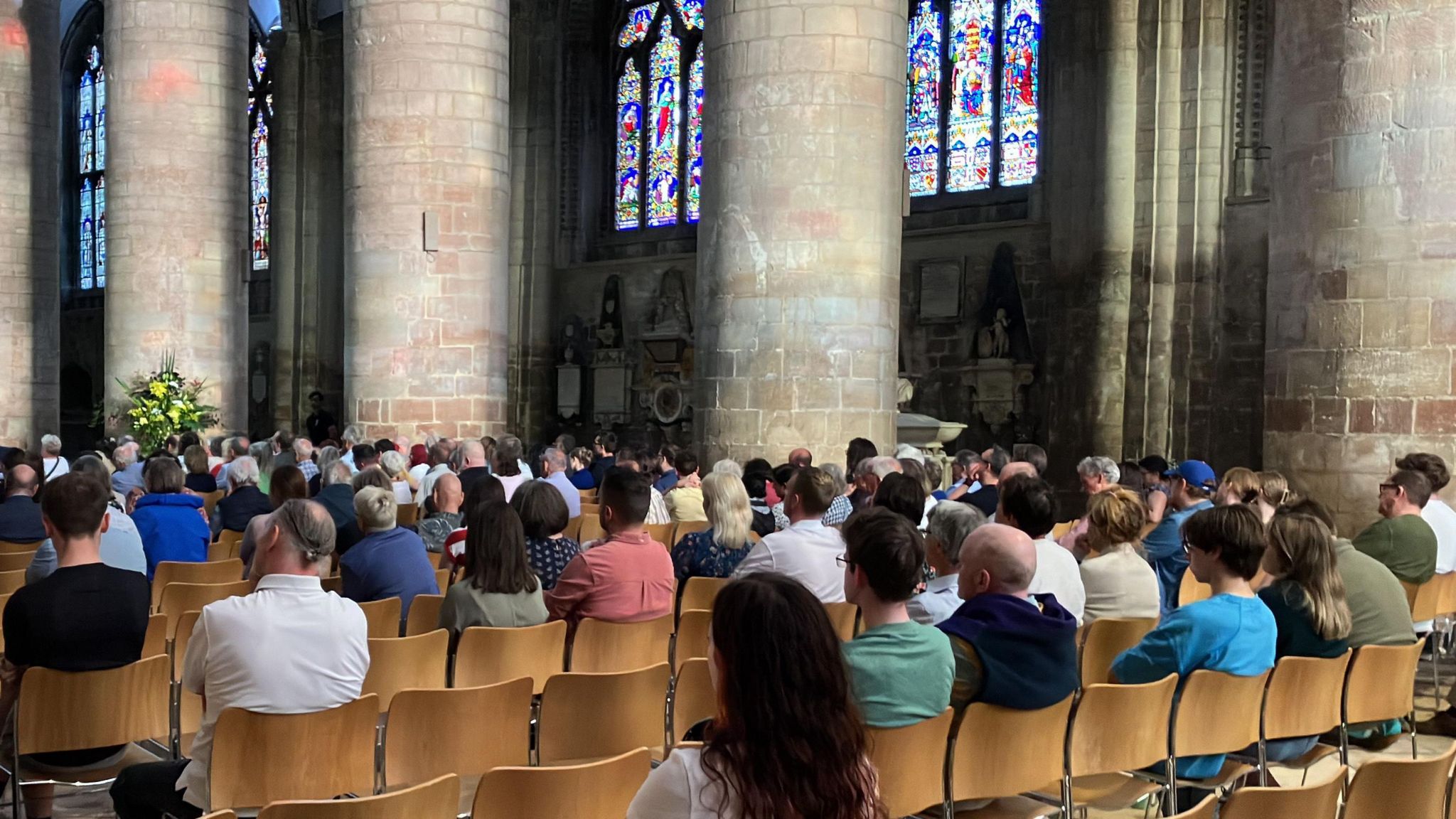 People sat on wooden chairs inside Gloucester Cathedral listening to candidates at the hustings