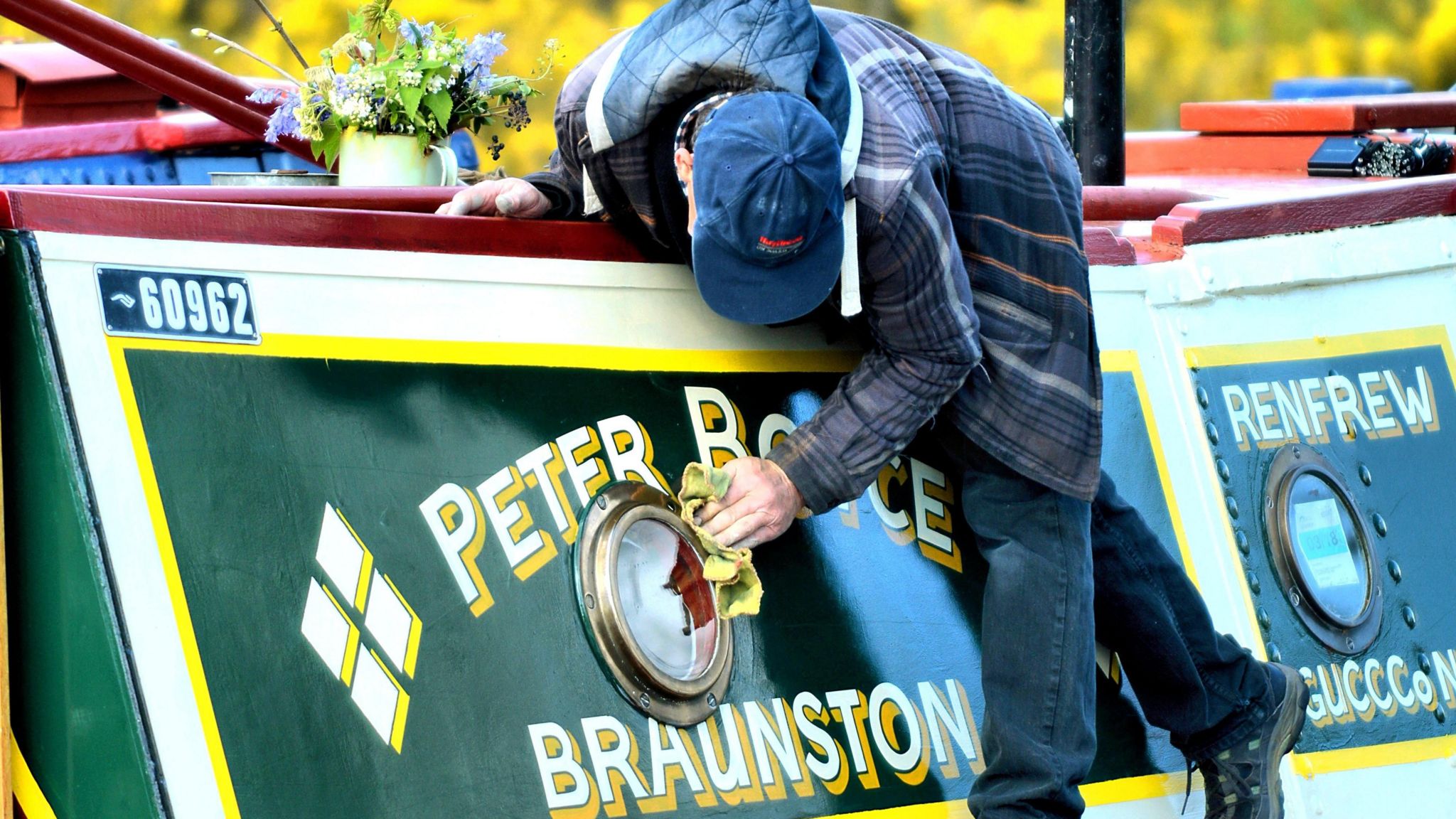 Man cleaning a green narrowboat with a yellow rag