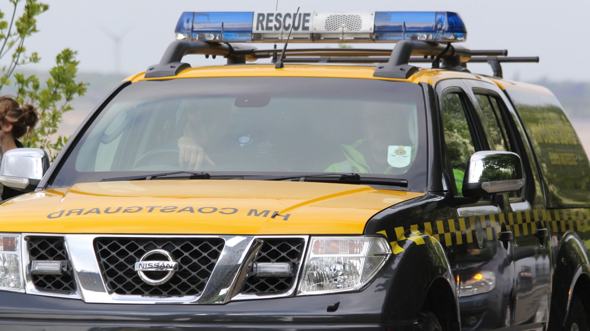 A black and yellow HM Coastguard vehicle with blue lights on its roof and two people sat inside.